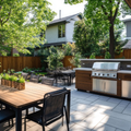 Backyard patio with dining table, grill, and lush trees beside a house