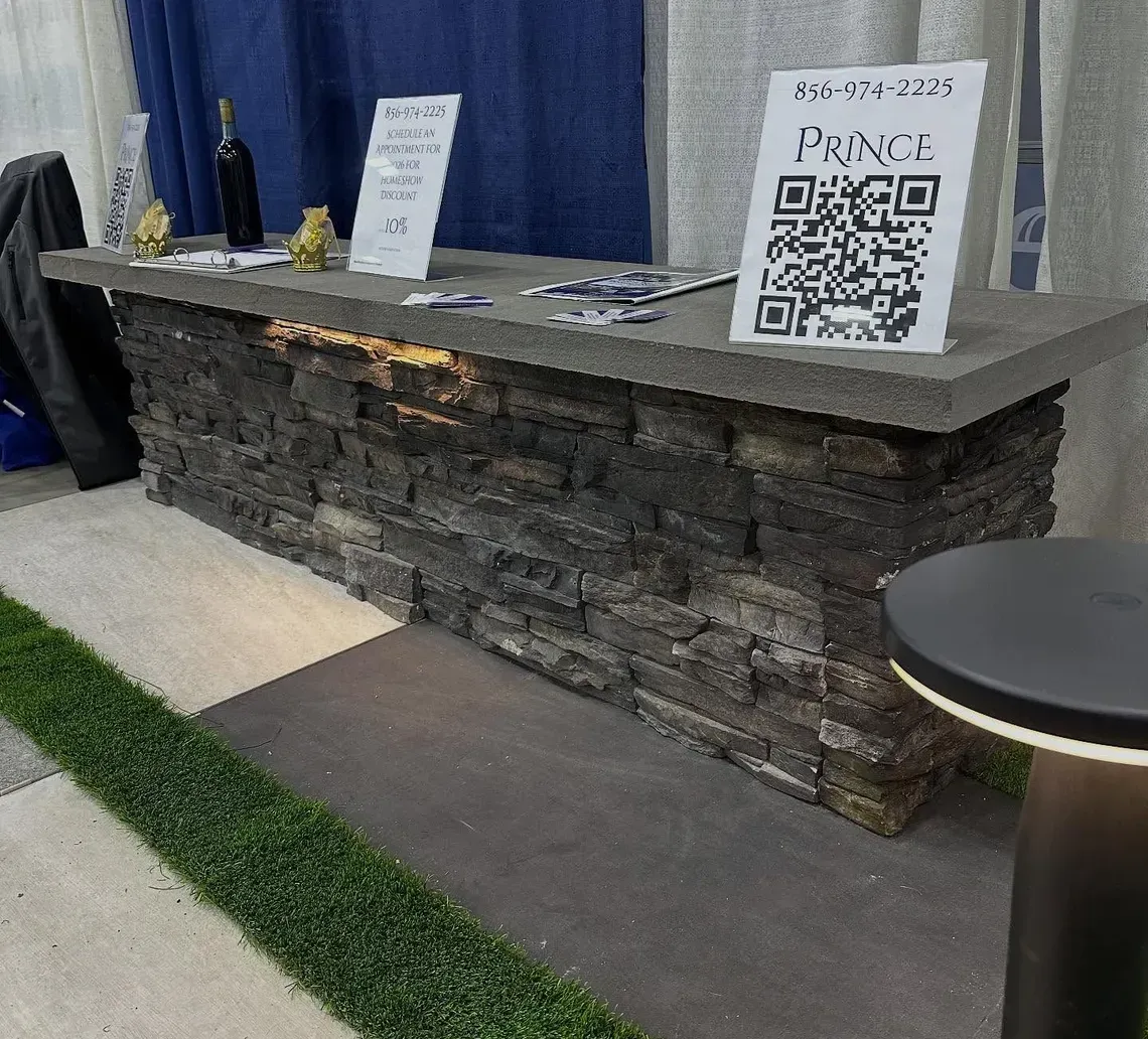 Stone-front bar counter with QR code sign, bottles, and blue drapes at an event booth