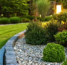 Curved stone border beside a lush green lawn and landscaped shrubs in a garden at sunset