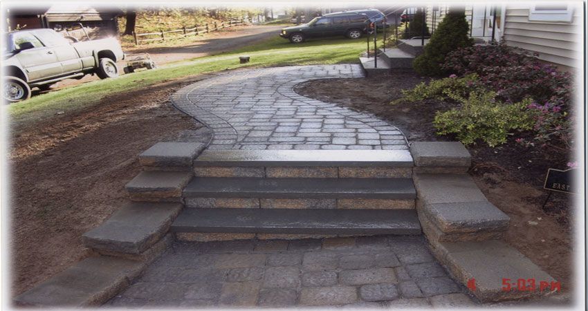 Front steps and a curved paved walkway leading to a house entrance, with parked cars nearby.