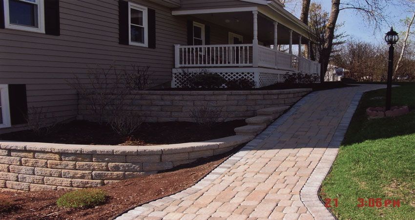 Stone walkway ramp leading to a house porch, with a retaining wall and winter lawn.