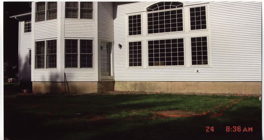 Suburban house exterior with white siding, large windows, and a lawn at night, timestamp in corner.