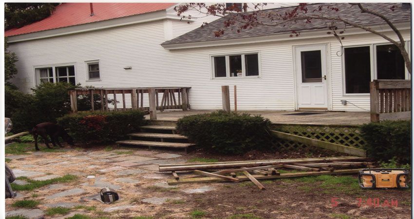 Flood-damaged backyard with debris, broken fence panels, and a white house in the background