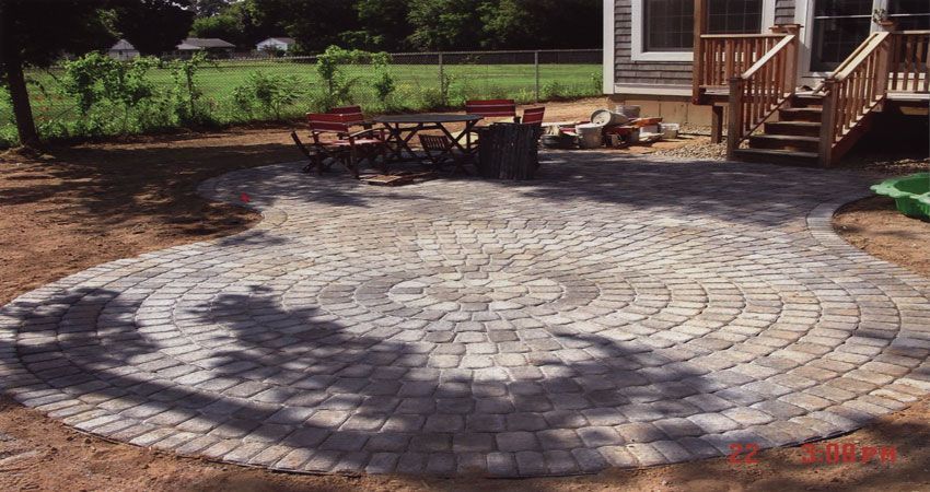 Circular stone patio with a swirling pattern beside a house and garden seating area