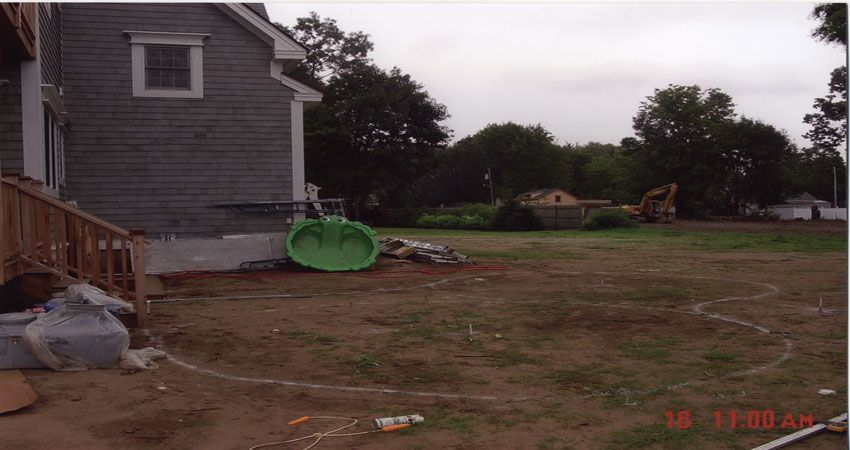 Partly built house beside a muddy yard with a green wheelbarrow and construction debris