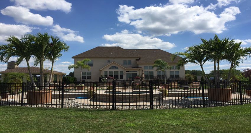 Large house with a fenced swimming pool, palm trees, and a bright blue sky with clouds.