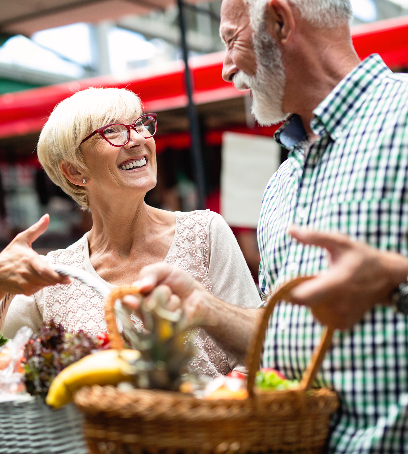 Smiling elderly couple at outdoor market, holding basket of produce.
