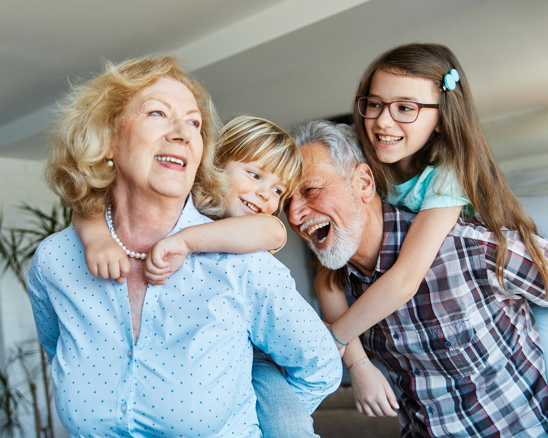 Grandparents giving piggyback rides to grandchildren, laughing indoors.