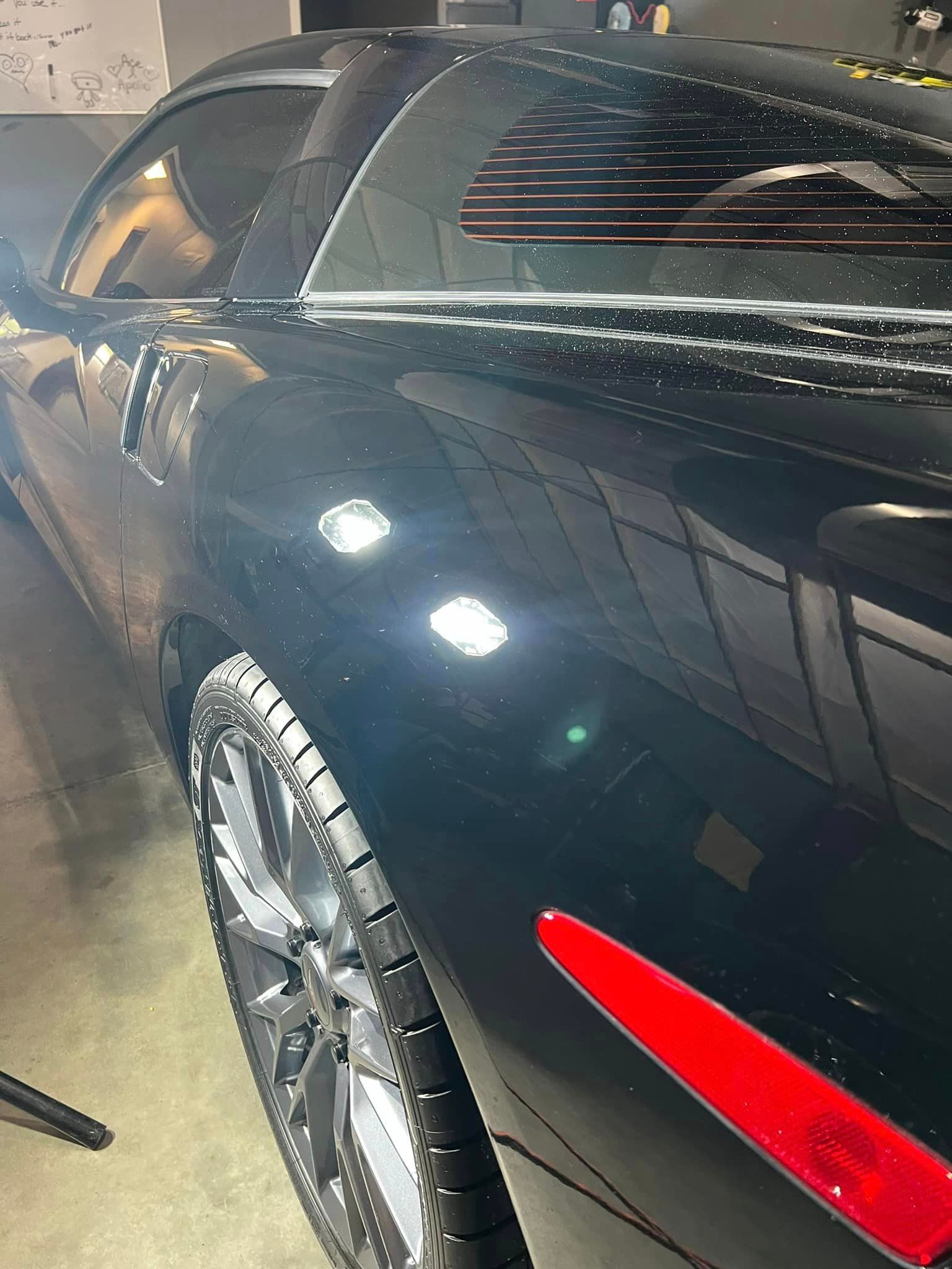 A black car with a red tail light is parked in a garage.