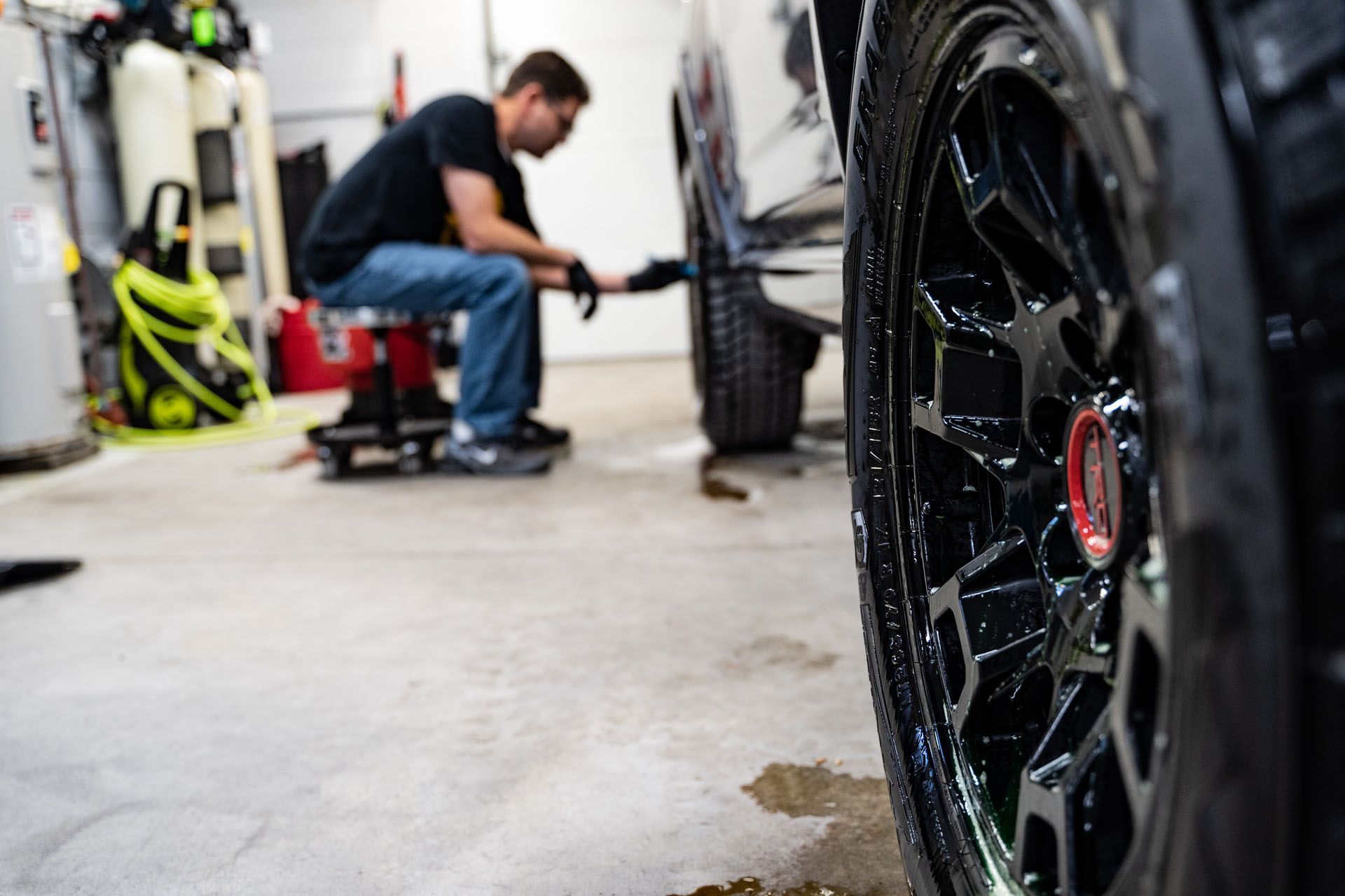 A man is cleaning the tires of a car in a garage.
