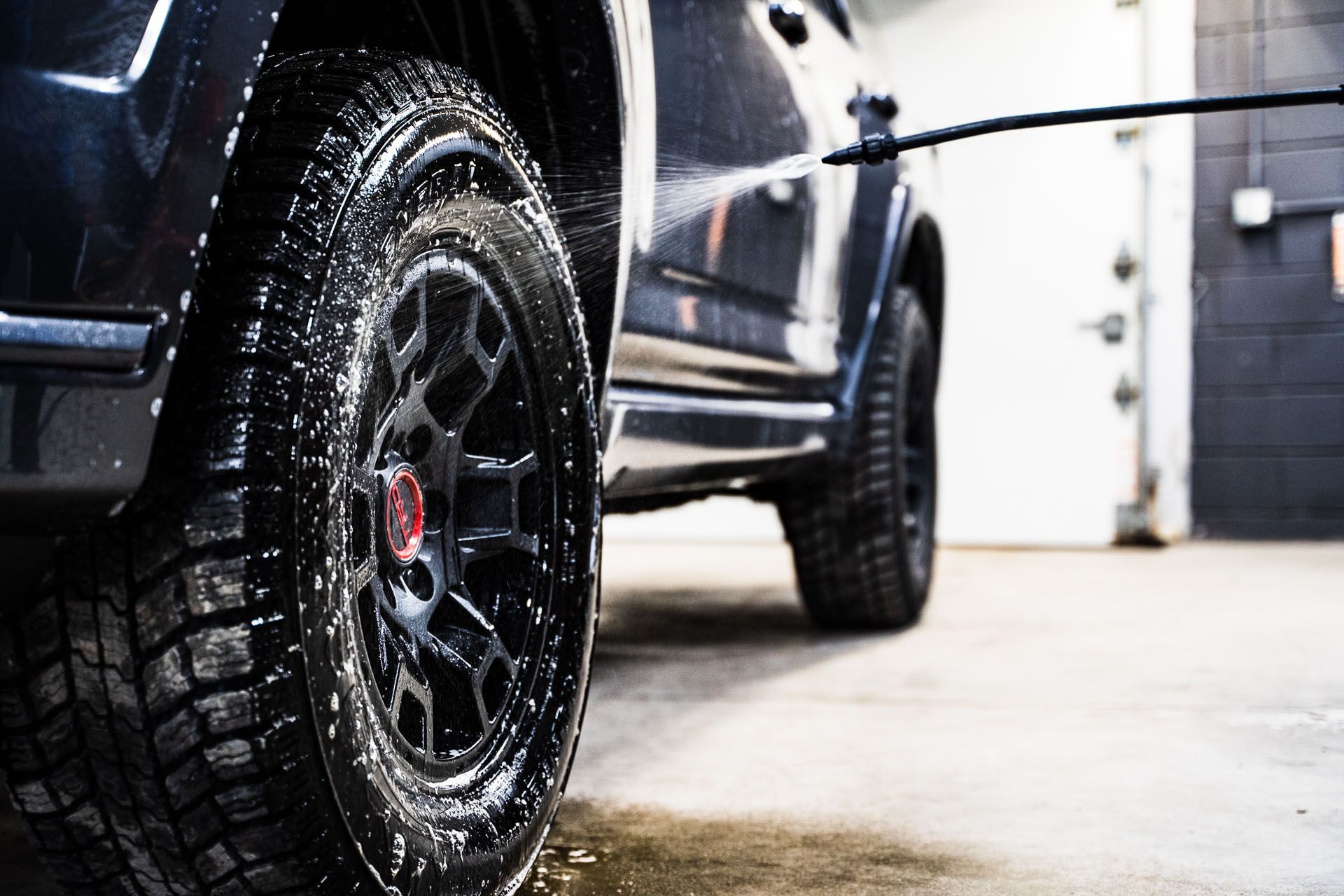 A car is being washed with a high pressure washer in a garage.