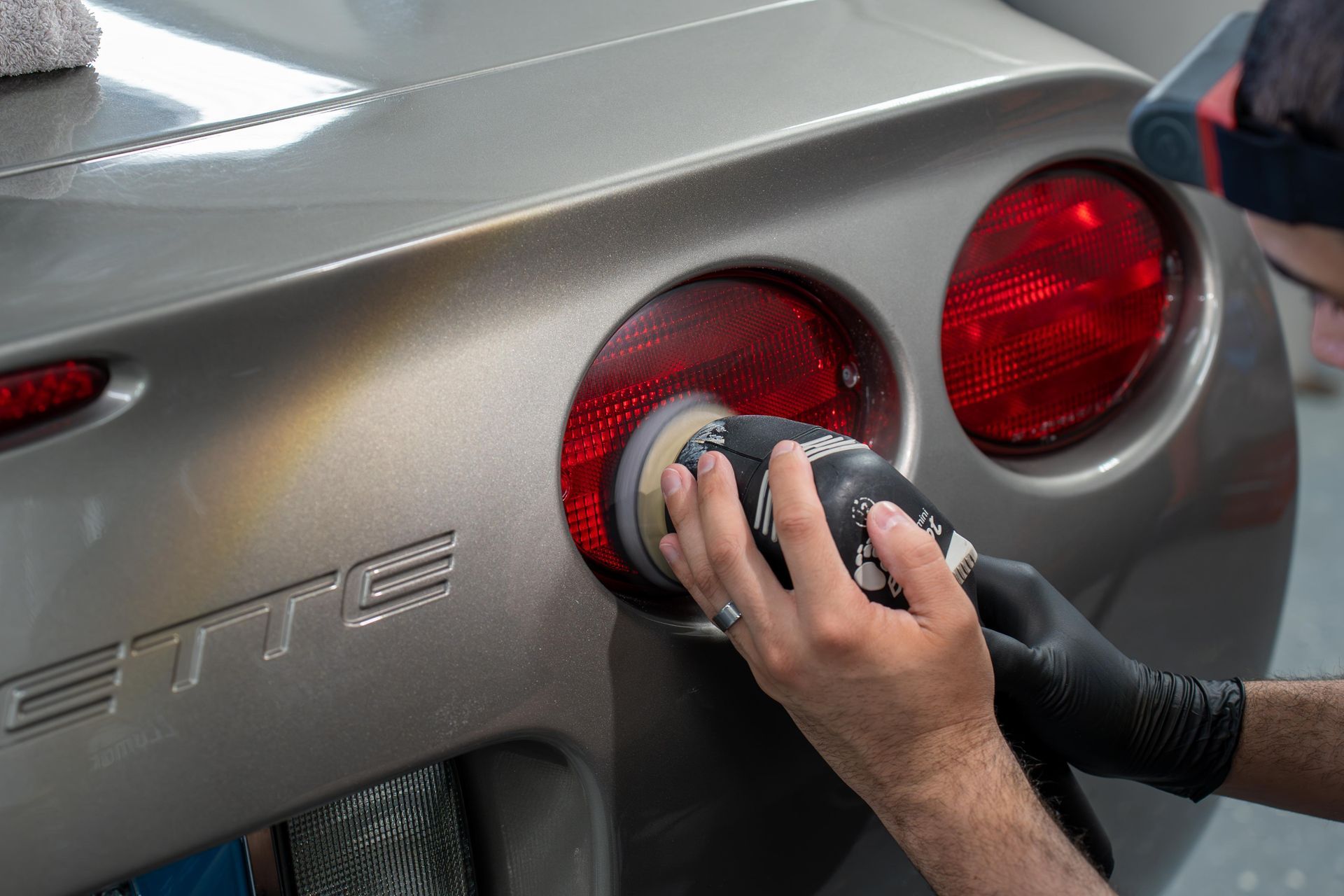 A man is polishing the tail light of a corvette.