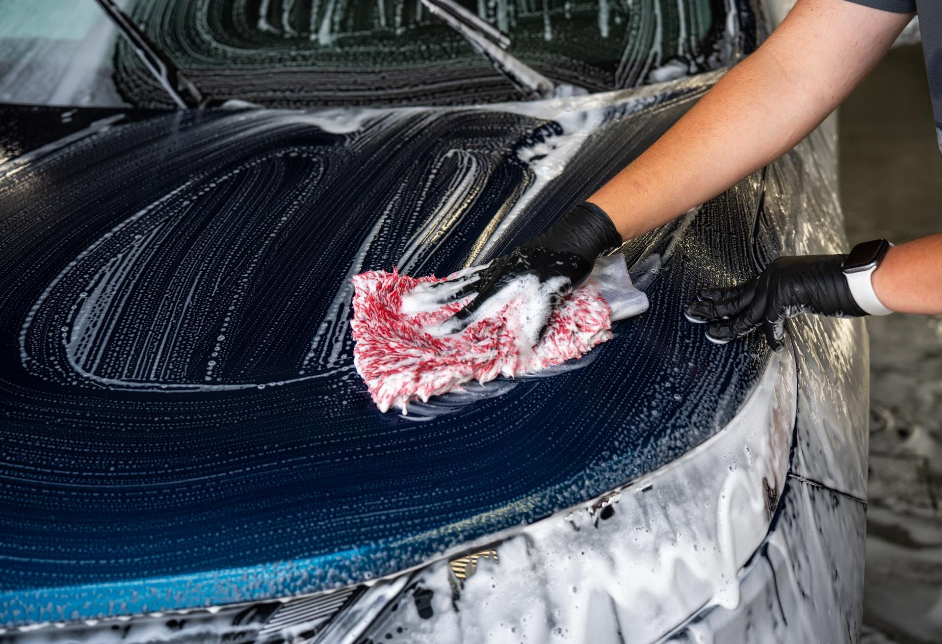 A person is washing a car with foam and a cloth.