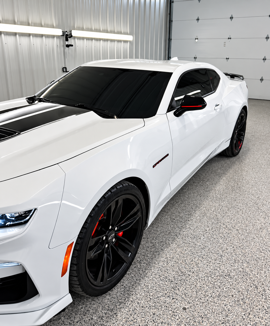 White sports car with black rims parked indoors in a garage, front-left view