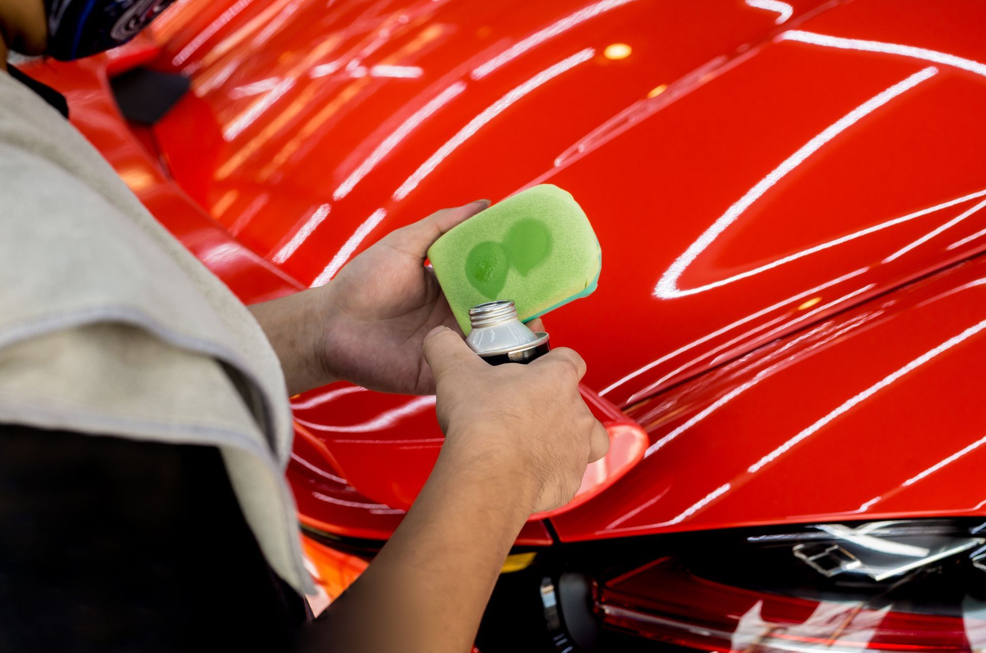 A person is polishing a red car with a sponge.