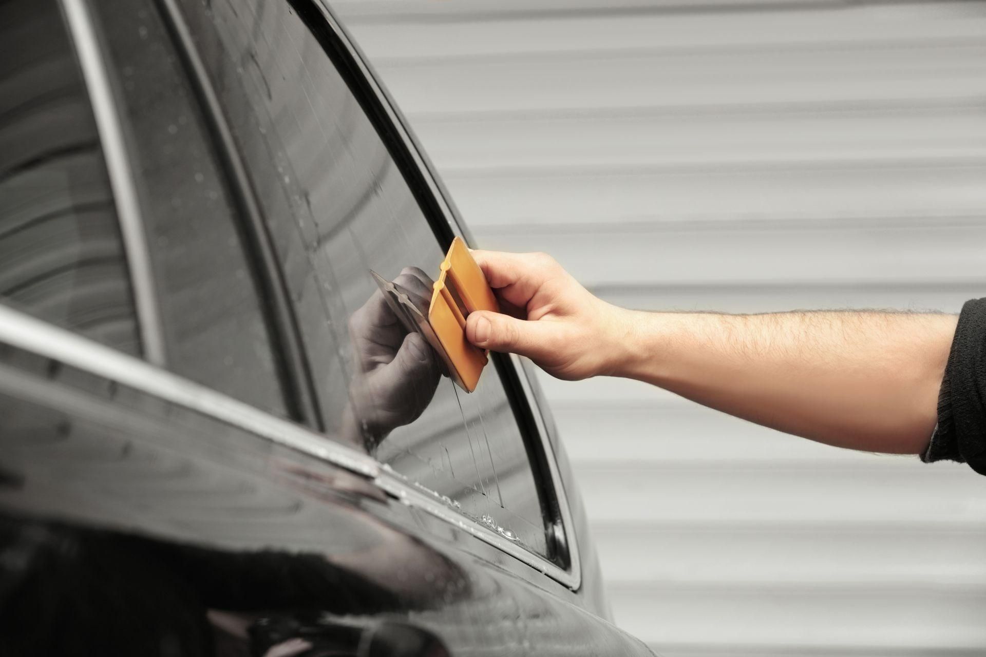 Hand cleaning a black car window with an orange cloth