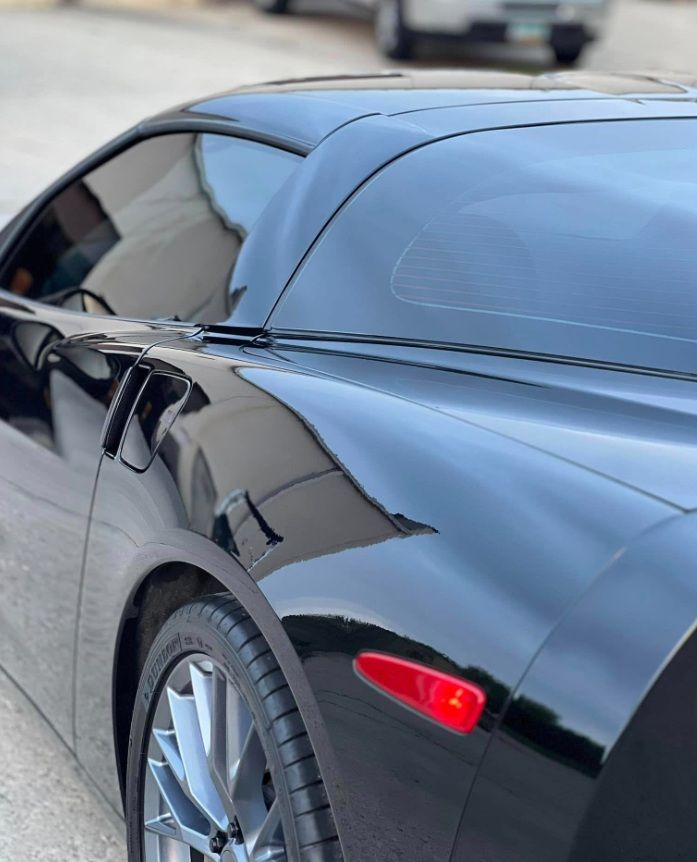 Close-up of a black sports car’s side and front wheel with a red side marker light.