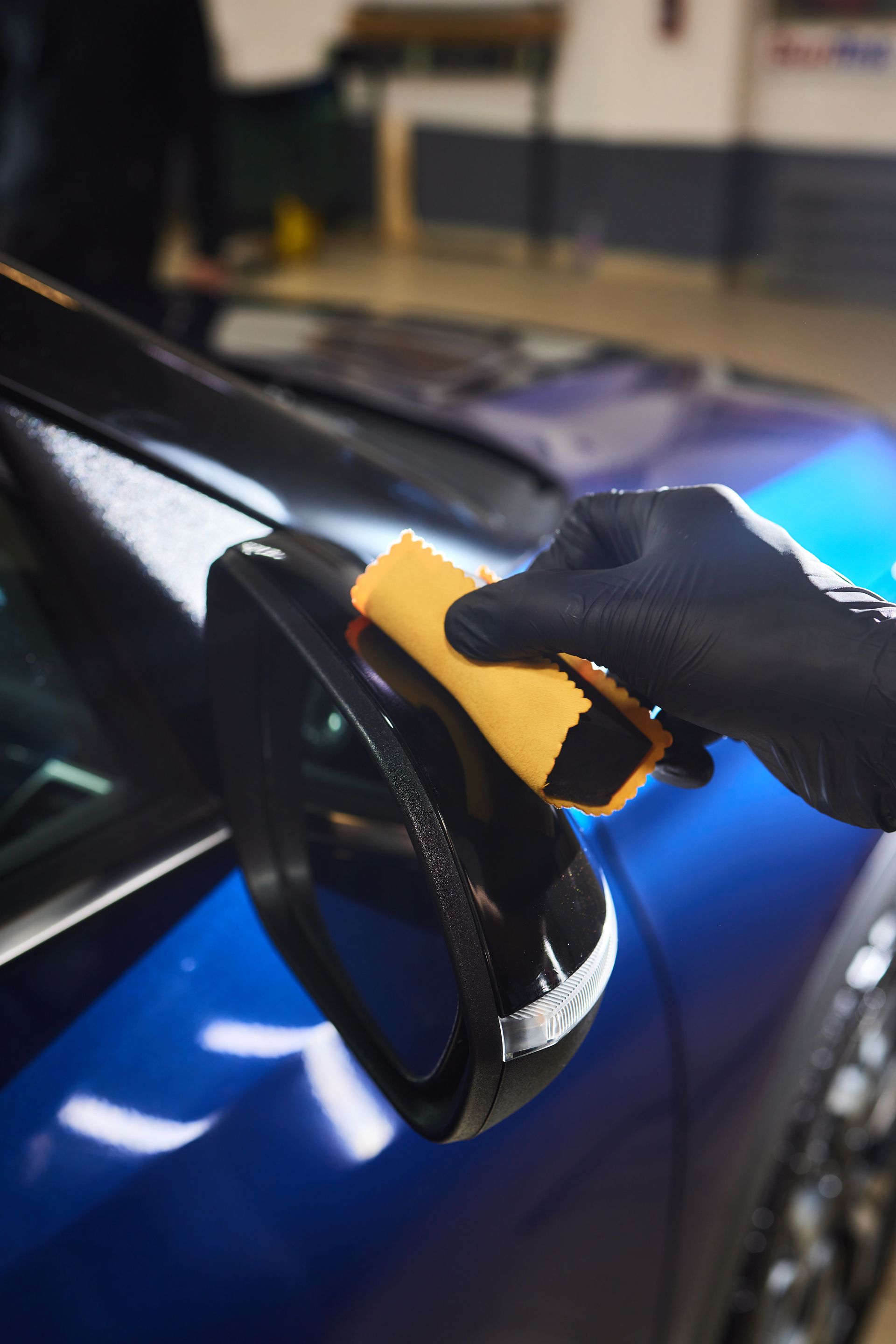 A person is cleaning the side mirror of a blue car with a sponge.