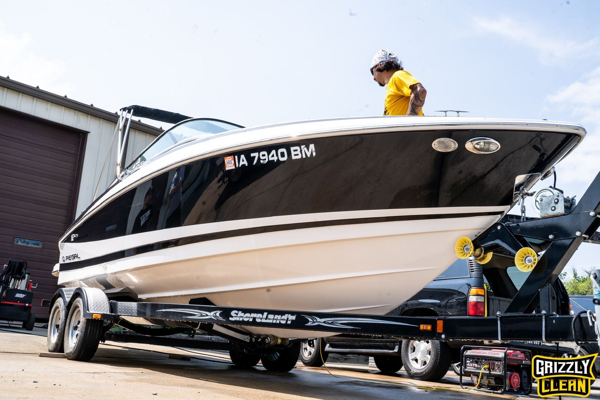 Black and white boat on trailer in a driveway, with a person in yellow on deck and a tow vehicle behind it
