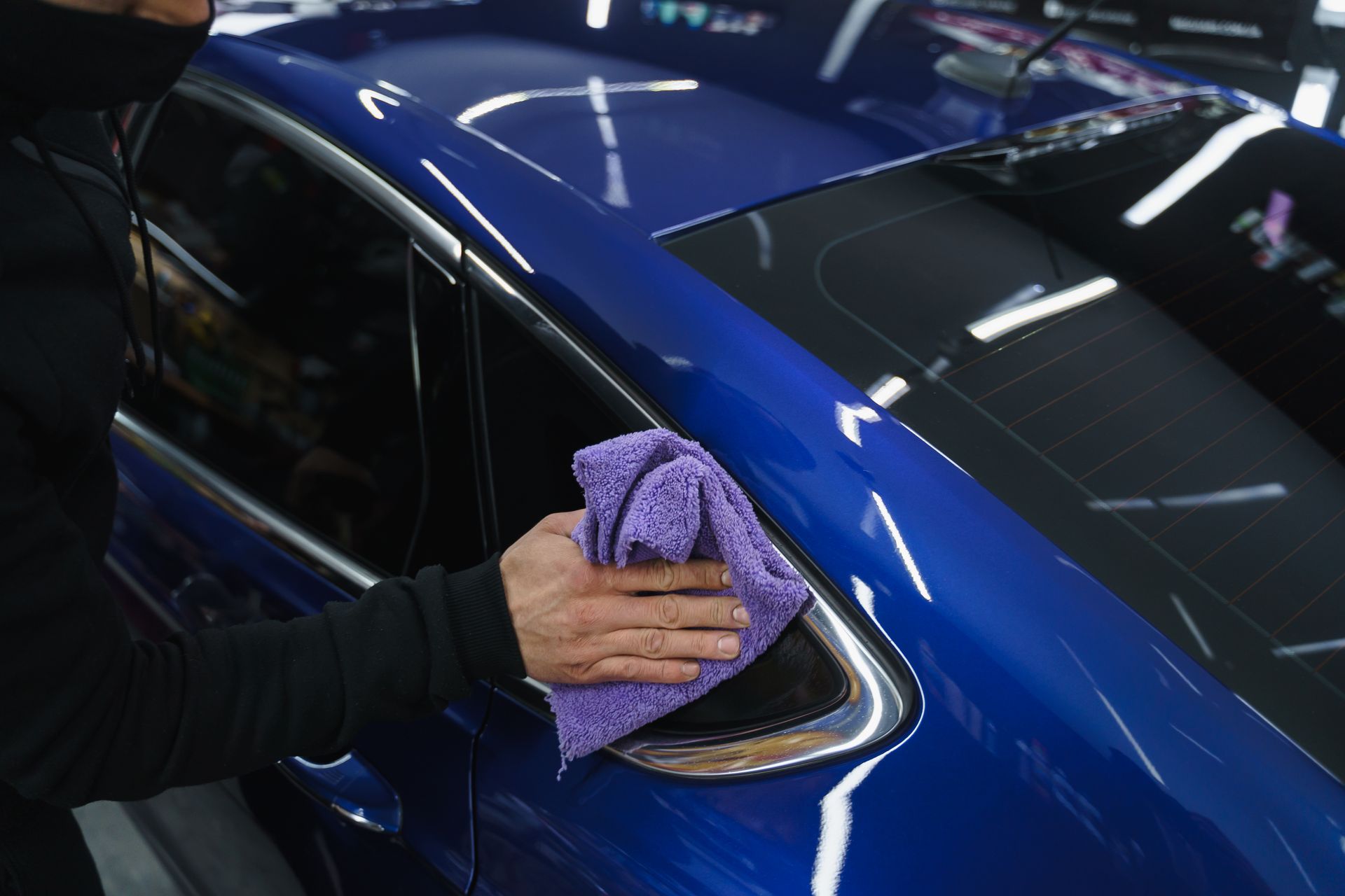 A person is cleaning a blue car with a towel.