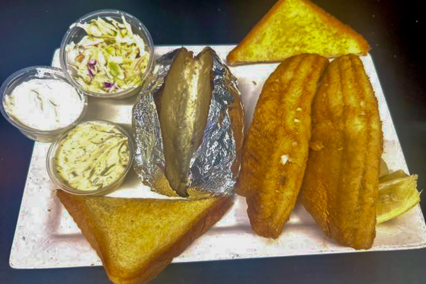 Plated fried fish meal with coleslaw, sauce cups, and toasted bread slices on a white tray.