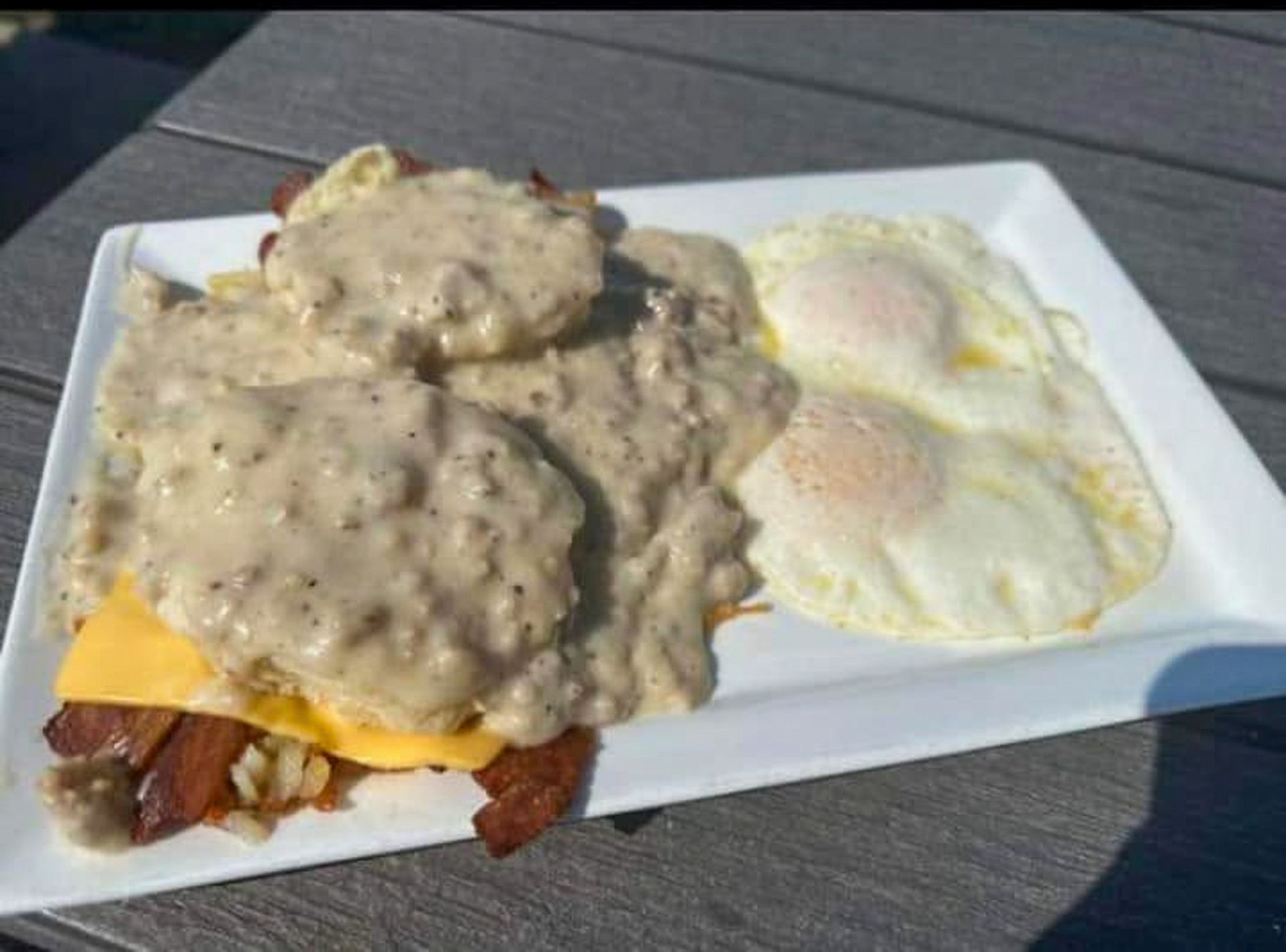 Breakfast plate with biscuit, gravy, cheese, bacon, and two fried eggs