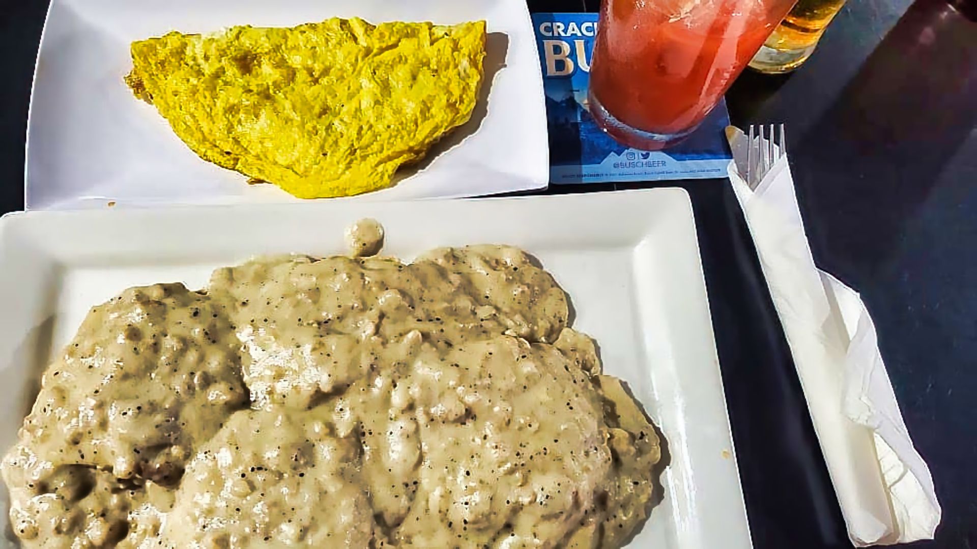 Plate of biscuits and gravy with a yellow omelet on a cafeteria tray and a red drink