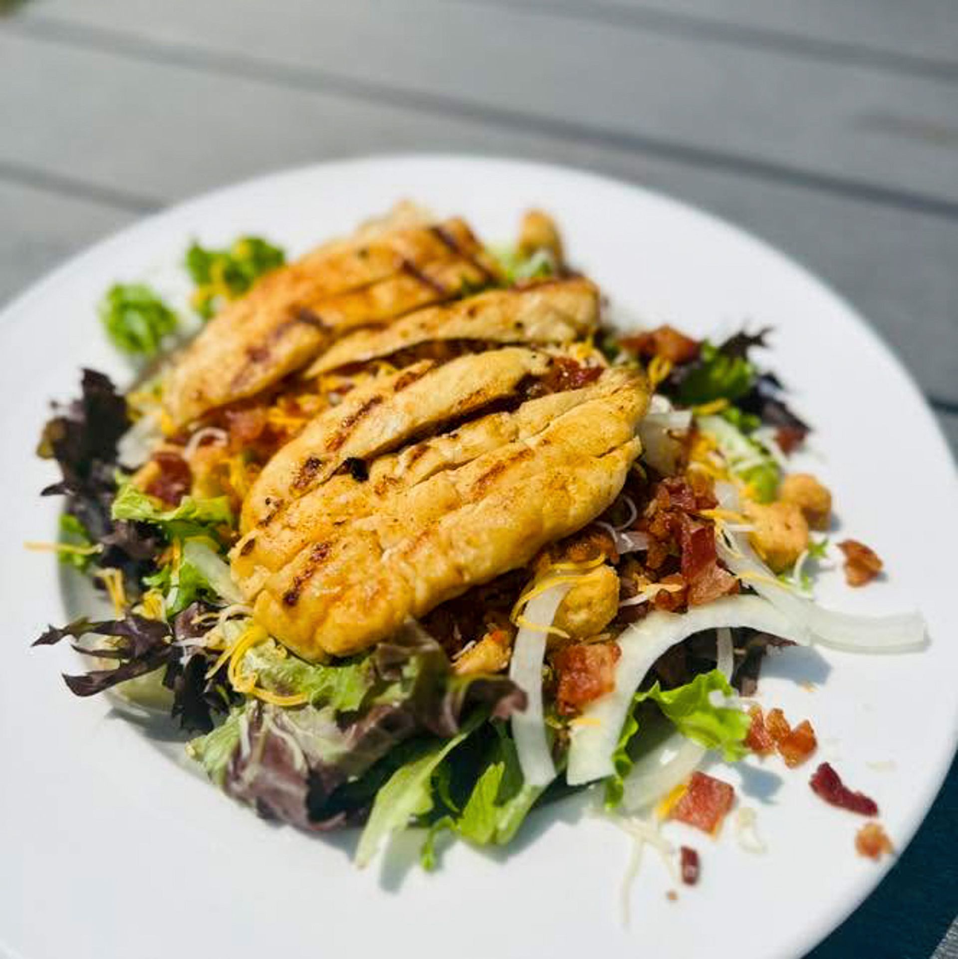 Grilled chicken breast slices on mixed greens with vegetables and dressing on a white plate