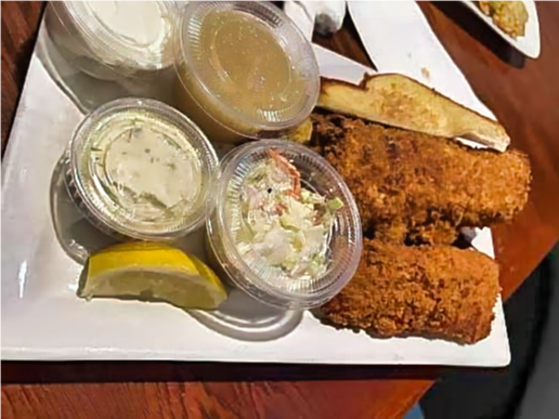 Fried fish plate with coleslaw, tartar sauce, and lemon wedge on a white tray