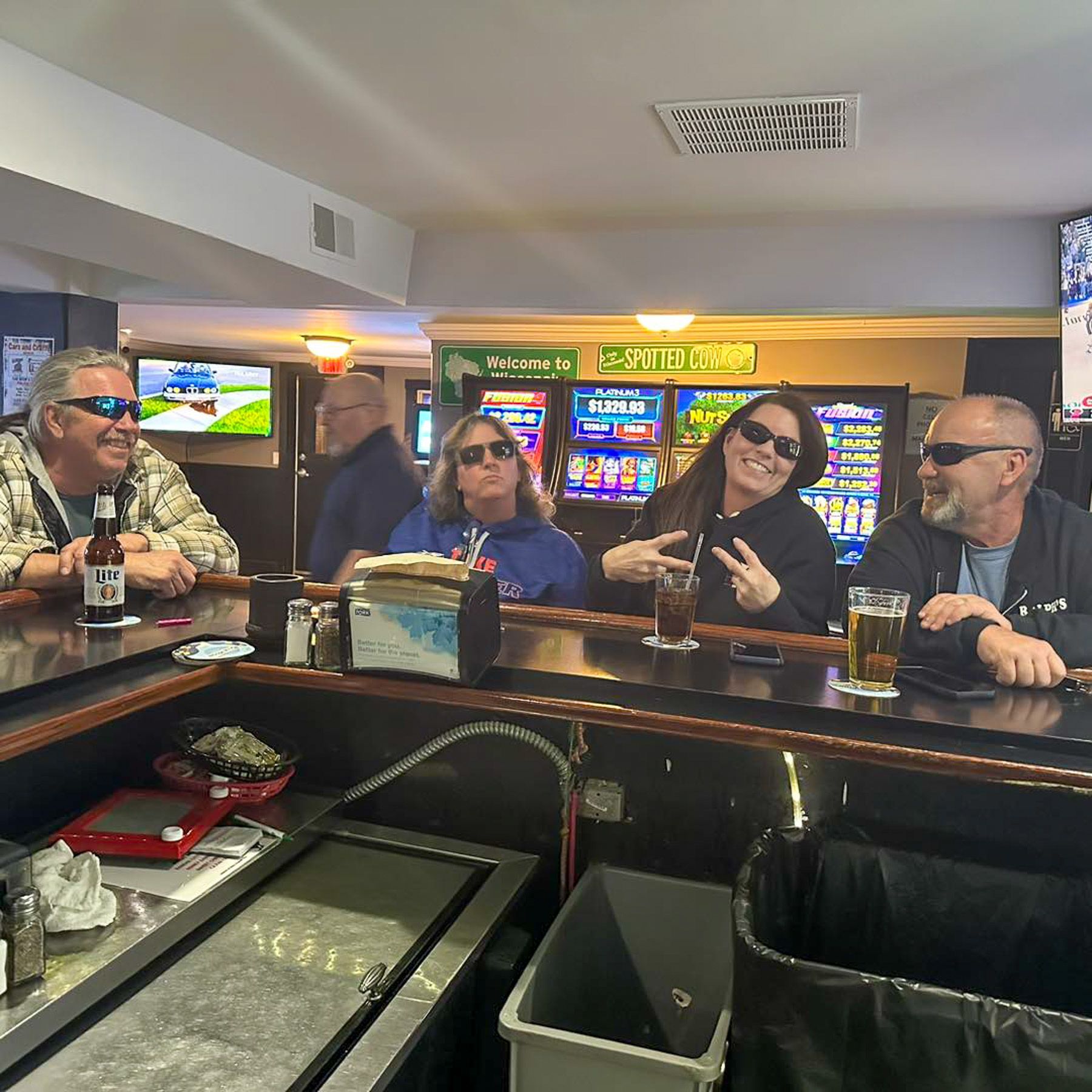 Four people seated at a casino bar with slot machines glowing in the background.