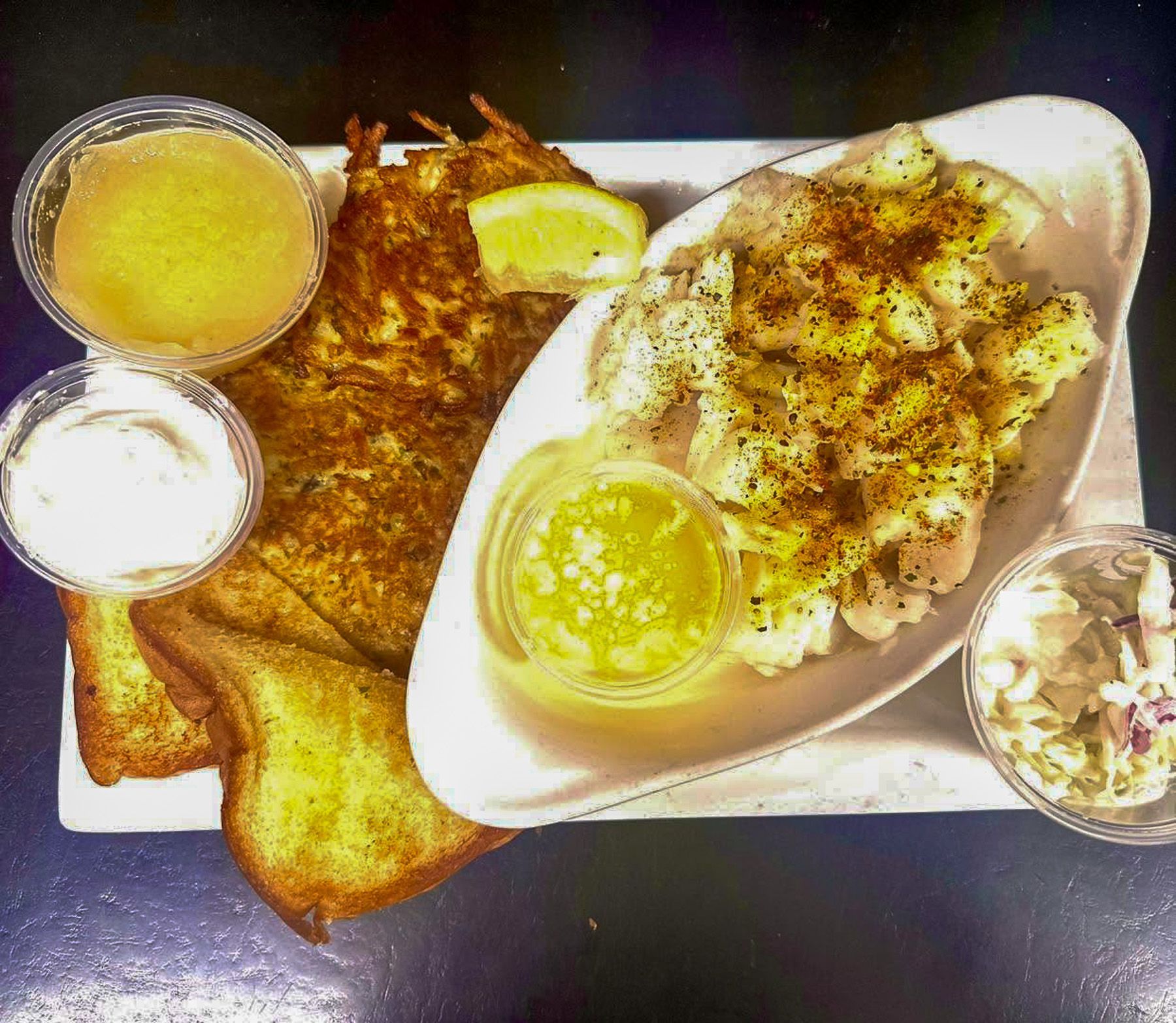 Assorted breakfast dishes: toast, eggs, and sides in takeout containers with dipping sauces.