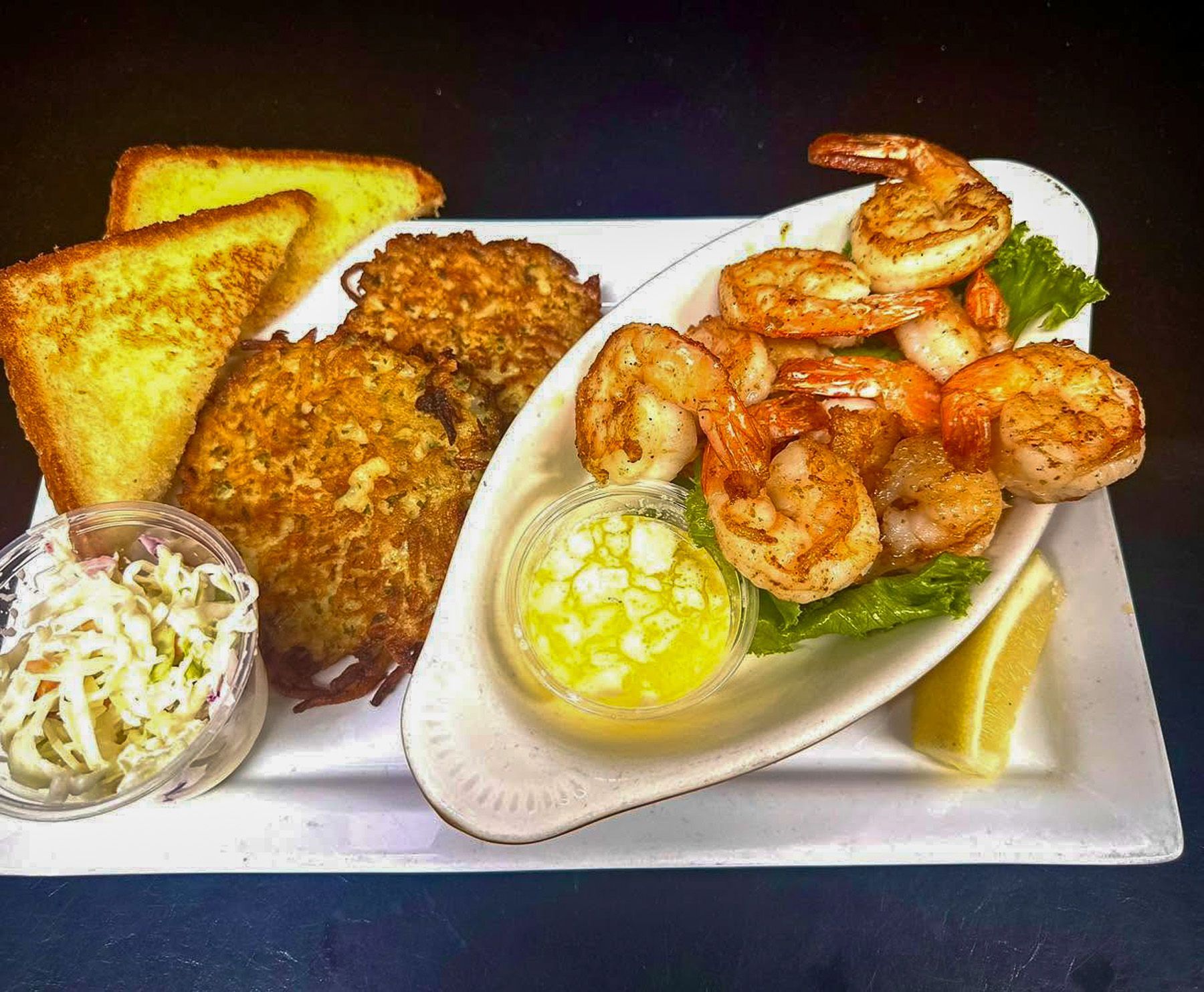 Fried shrimp, toast, grits, slaw, and lemon on a white plate, with two fried fish fillets