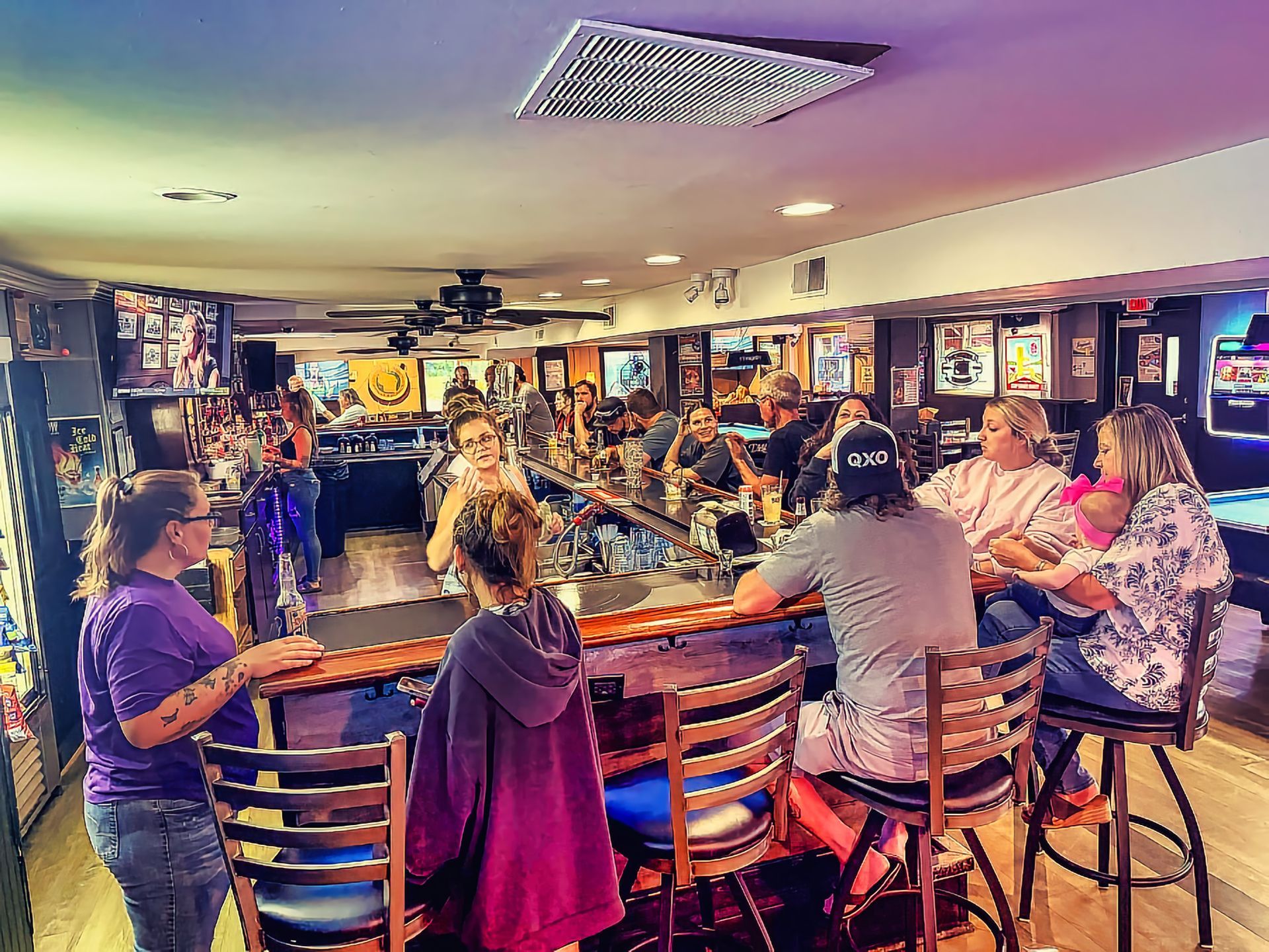 People seated at a bar in a lively, neon-lit pub with stools and wall decor.
