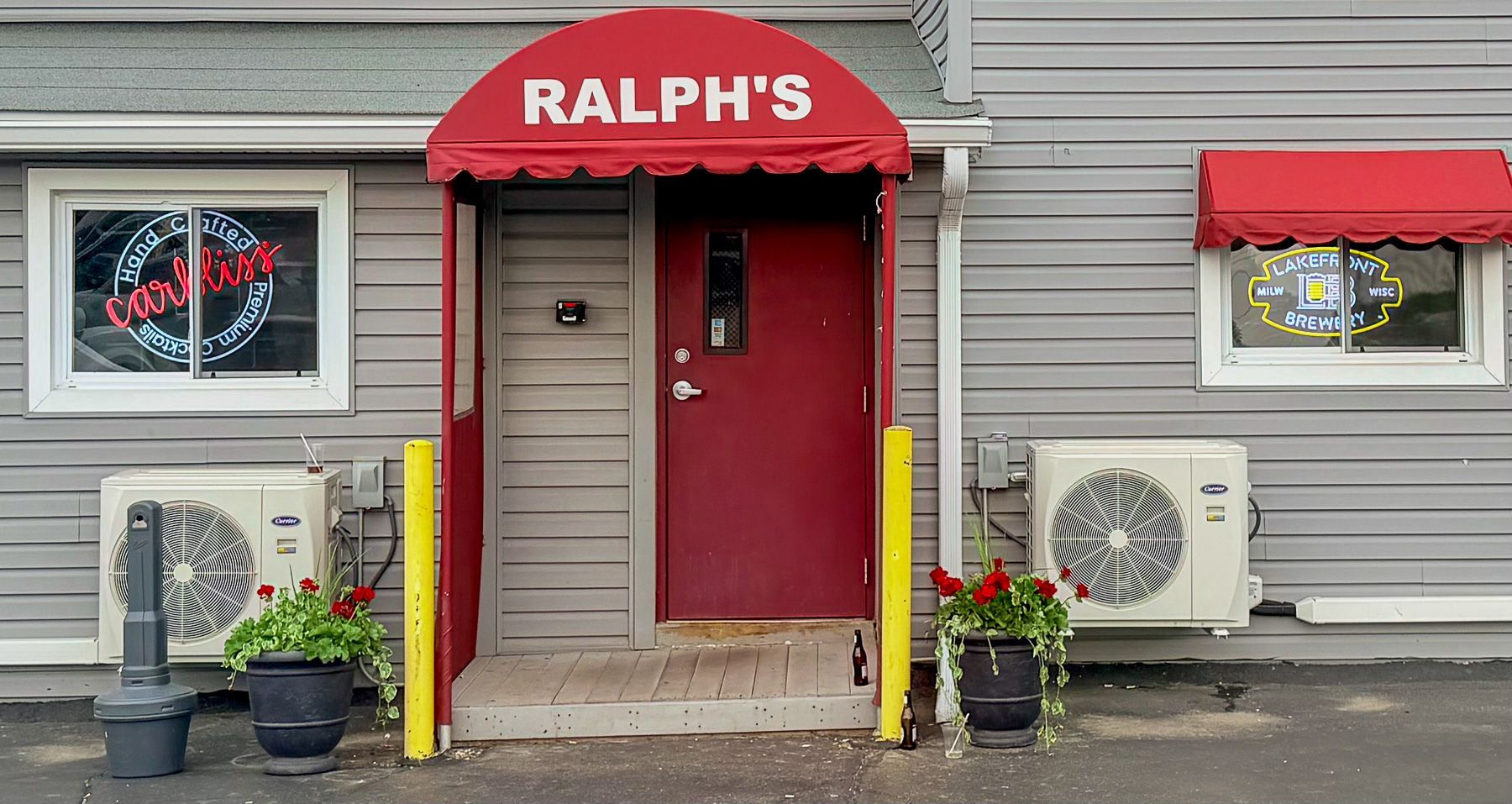 Front entrance of Ralph’s with red awning, red door, beige siding, and potted plants