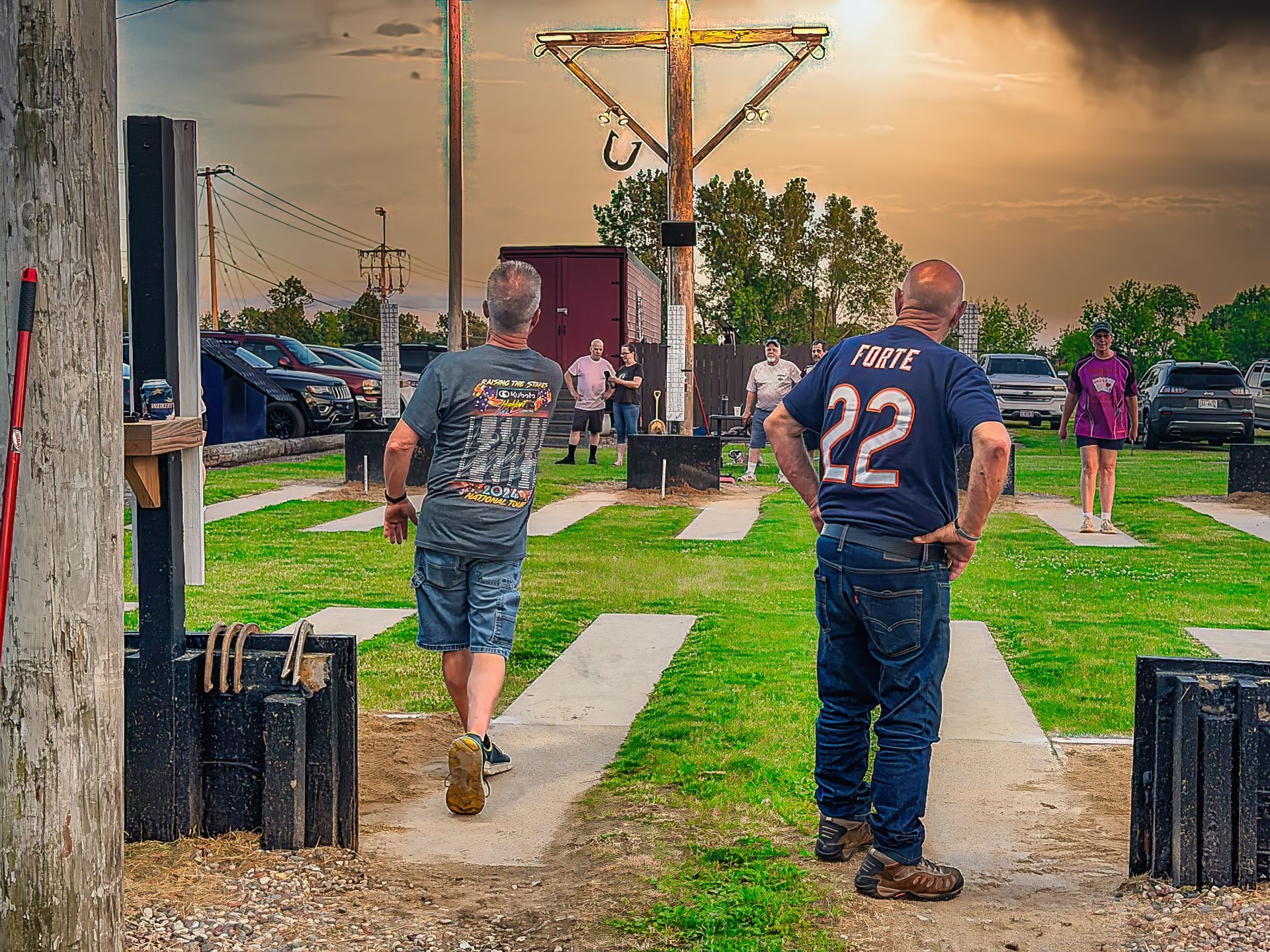 People standing outdoors in a grassy park near a large wooden cross at sunset