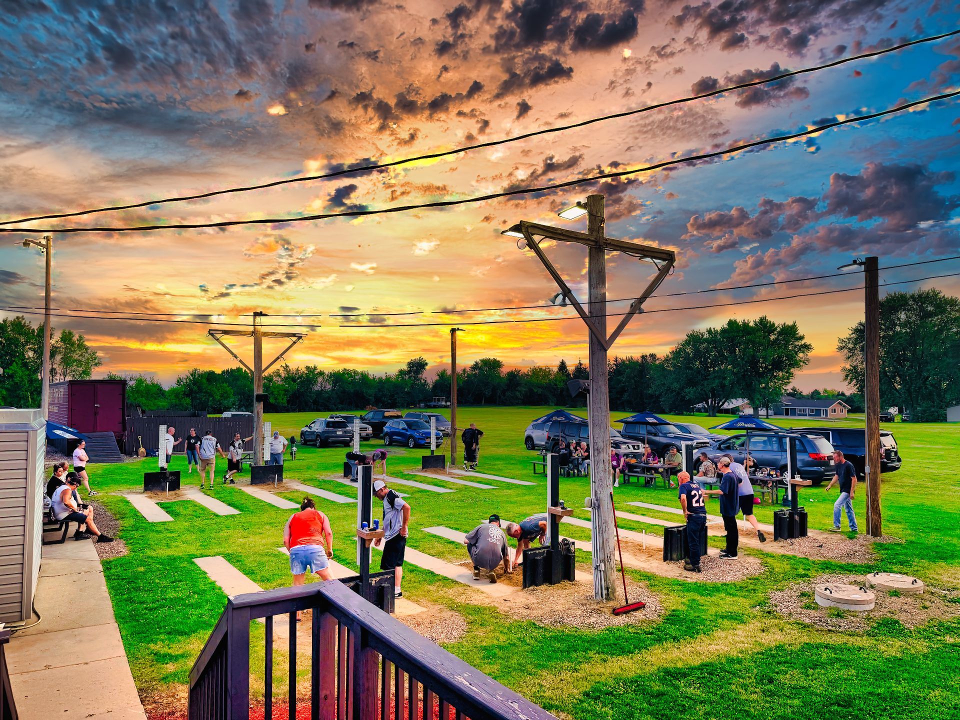 People relaxing in a park at sunset, with green grass, benches, and dramatic orange clouds overhead.