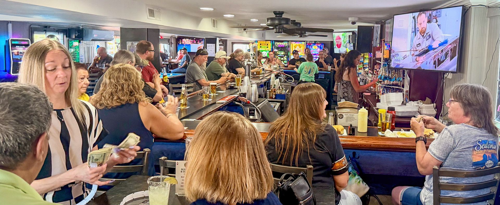 Crowded sports bar with patrons seated at tables, watching TVs and talking over drinks