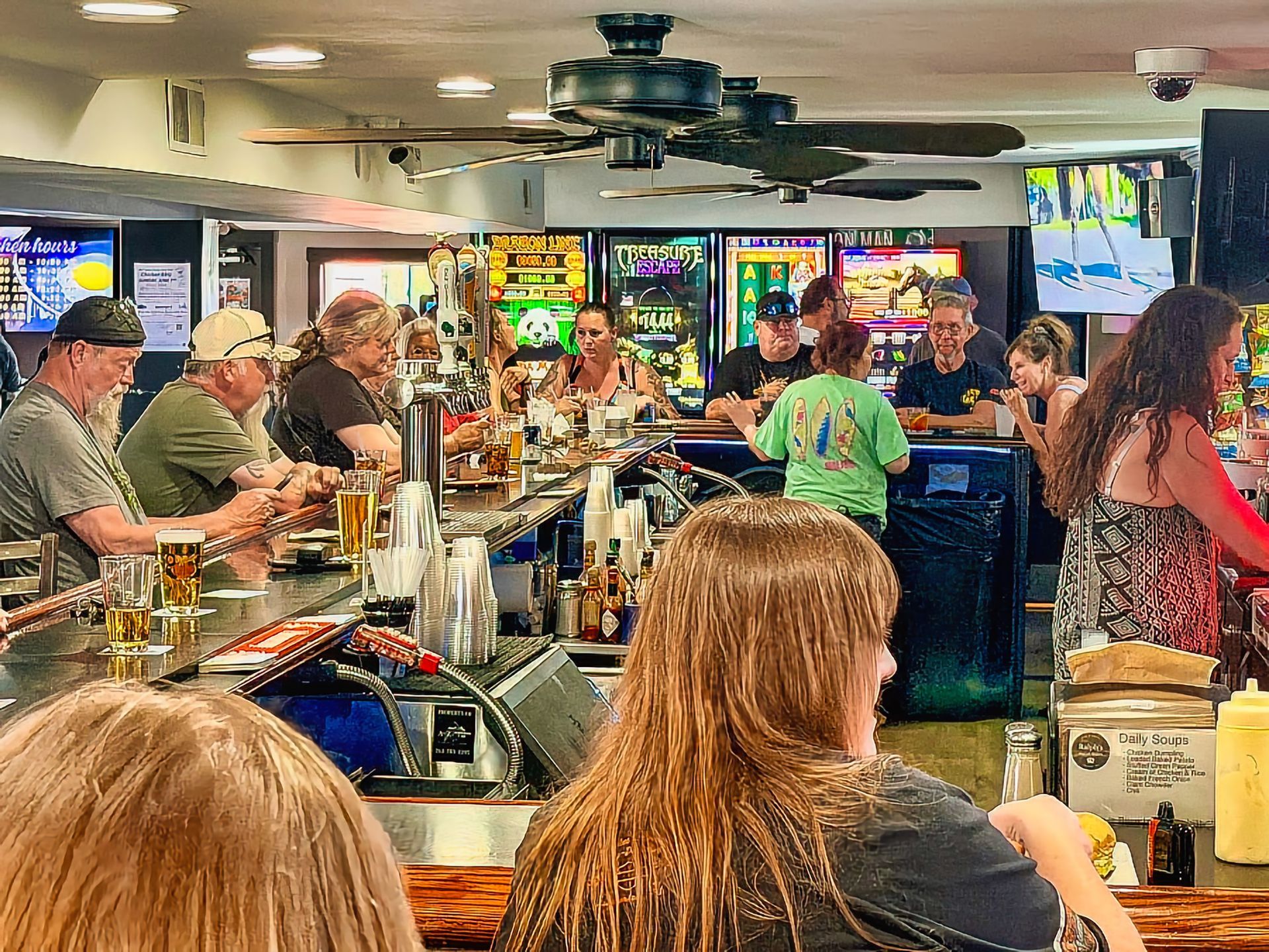 Crowded bar with patrons seated at the counter, TVs showing sports, and drinks on the bar