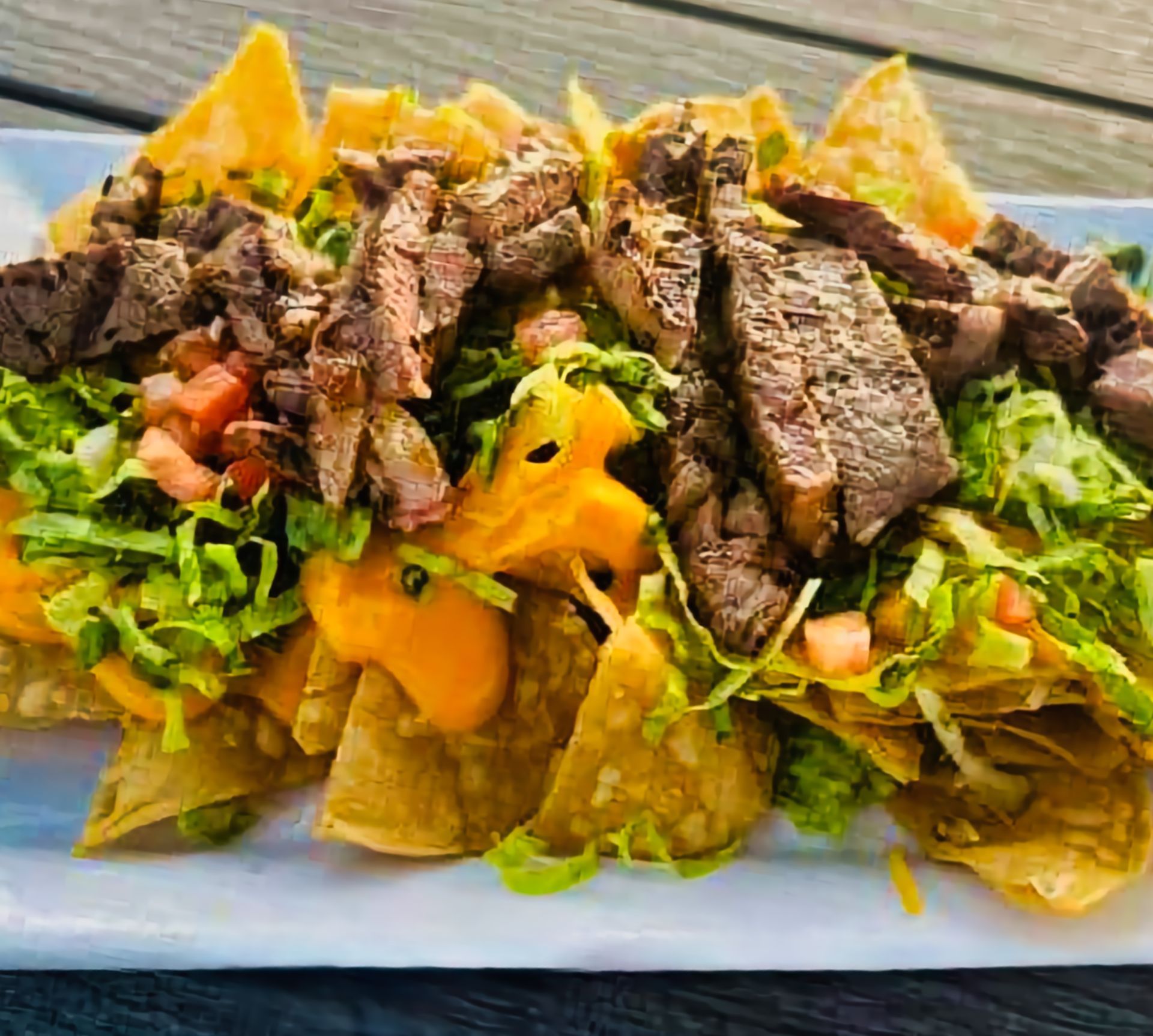 Loaded nachos topped with grilled steak, shredded lettuce, tomatoes, and melted cheese on a white plate