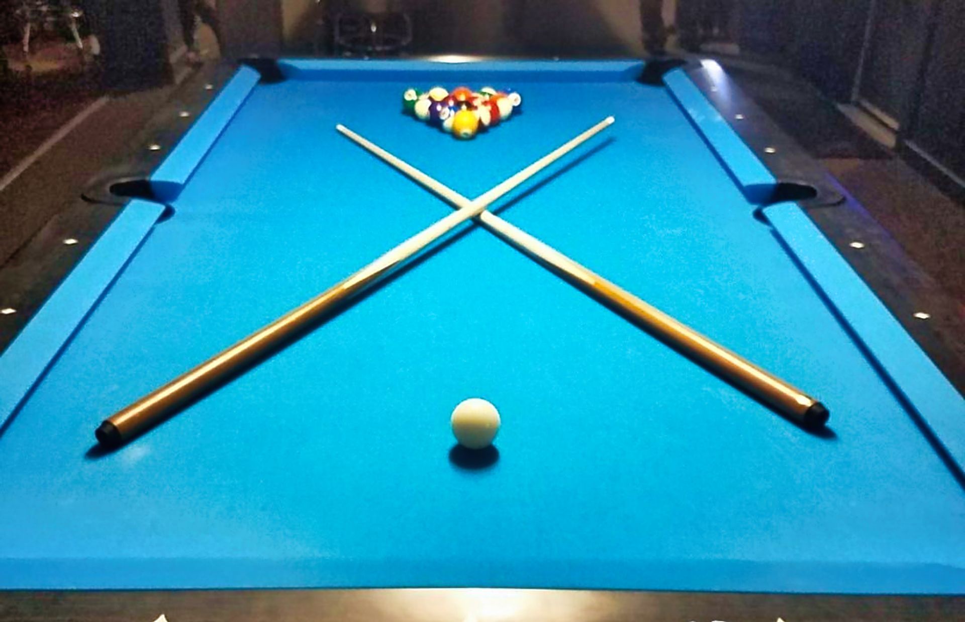 Pool table with blue felt, crossed cues, racked balls, and a cue ball near the front center