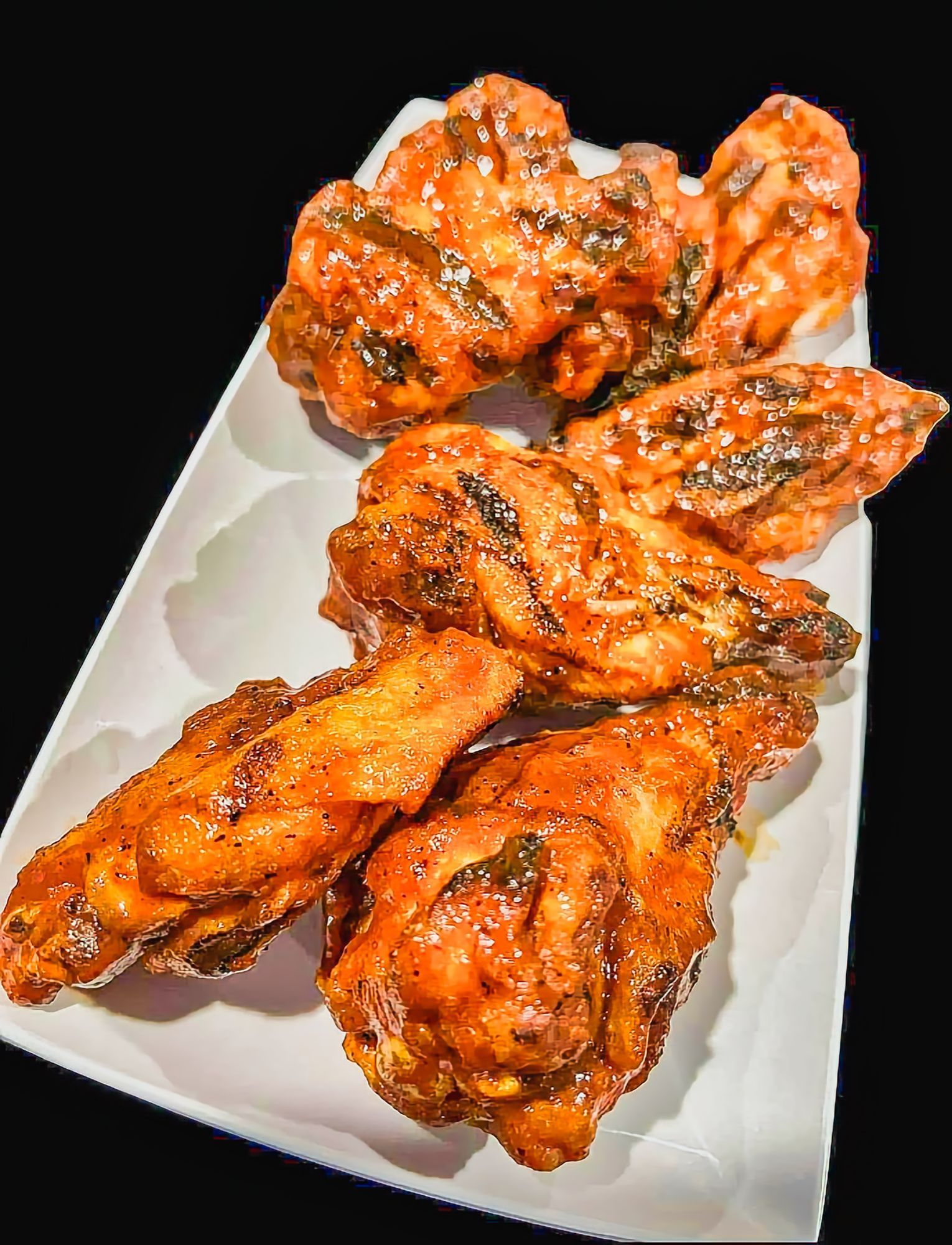 Platter of glazed, charred chicken wings in orange sauce