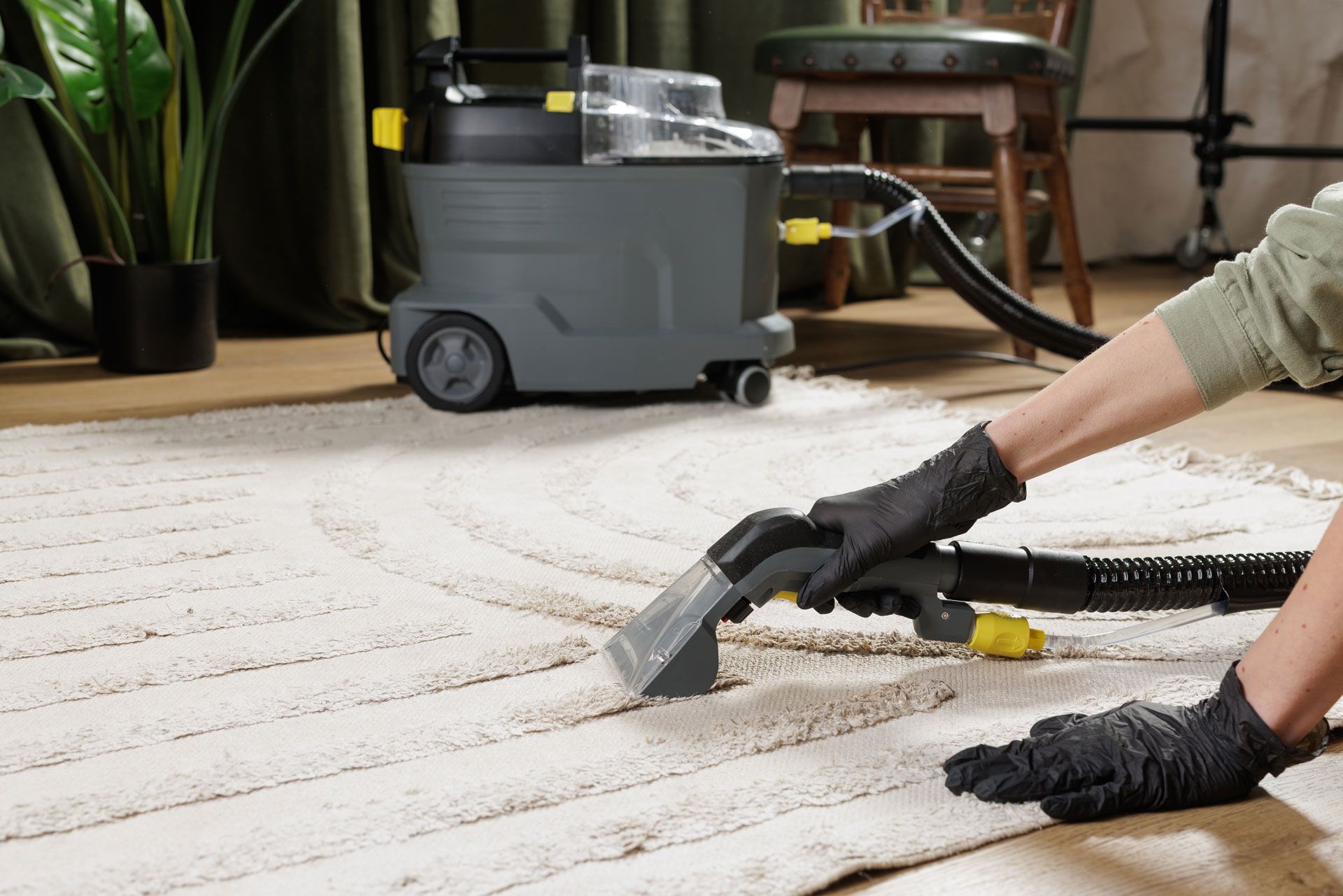 Person vacuuming a light rug with a handheld cleaner beside a gray carpet extractor in a living room