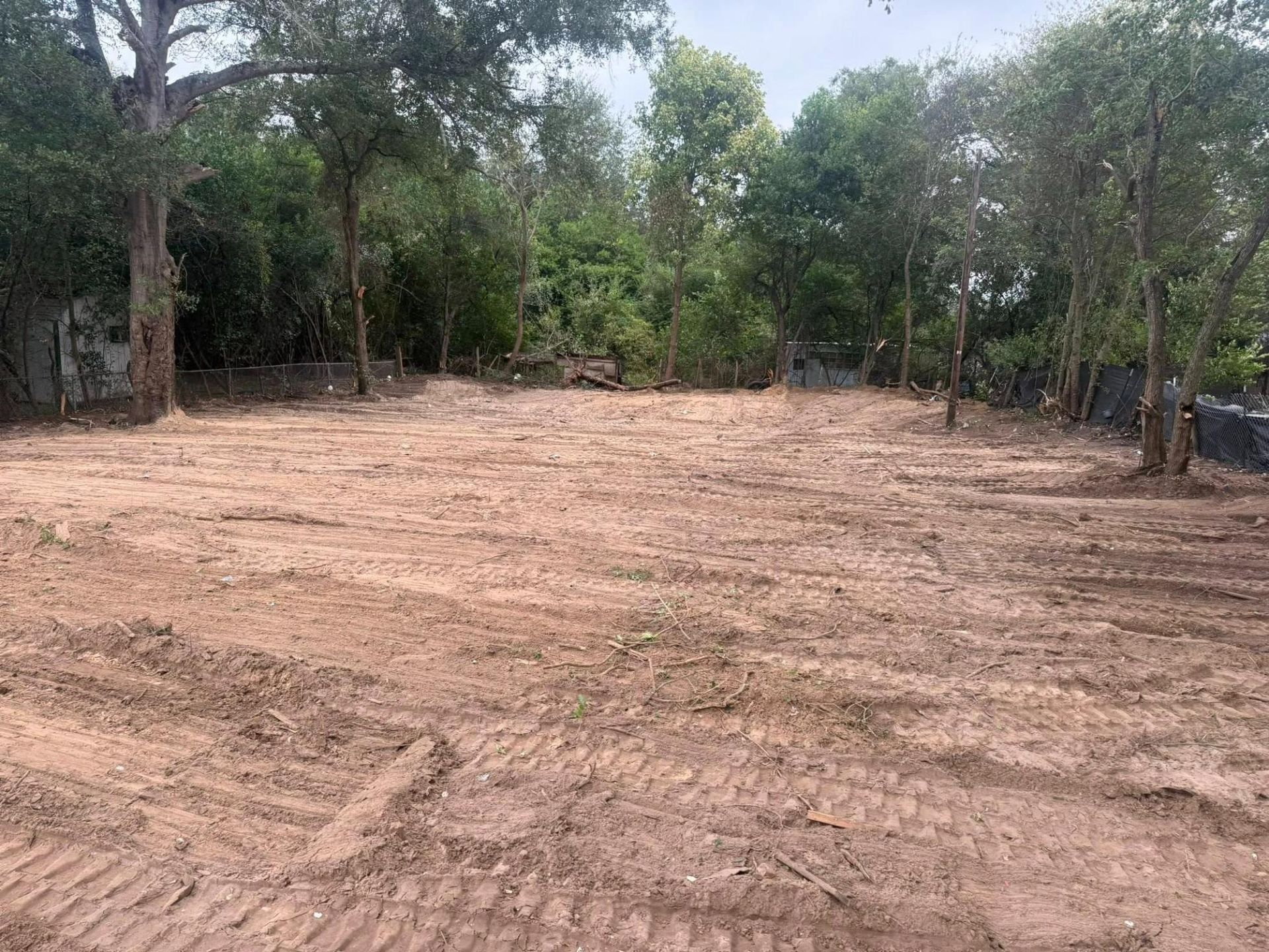 Cleared dirt lot with tire tracks, surrounded by trees.