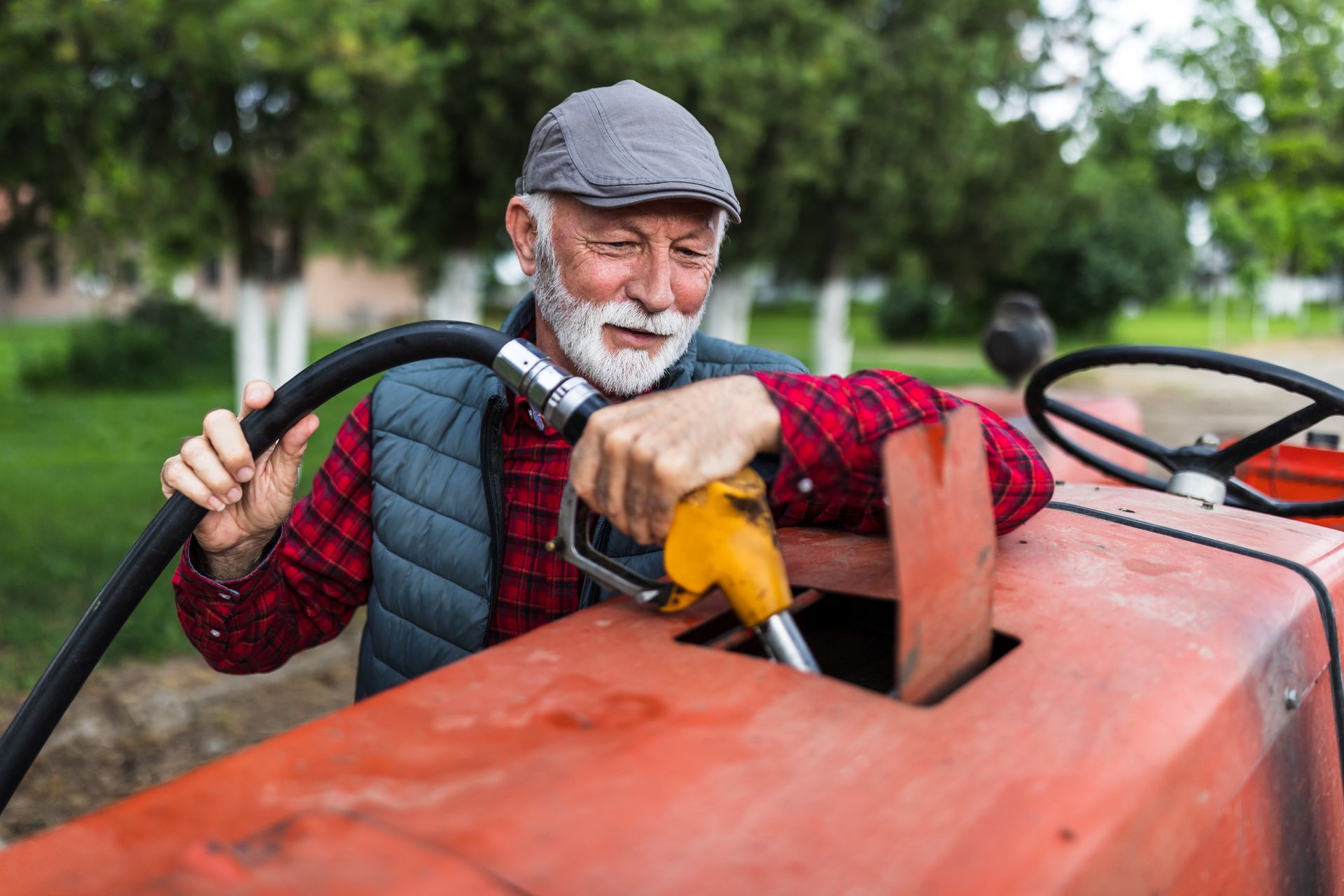 Farmer fueling tractor with yellow nozzle outdoors.