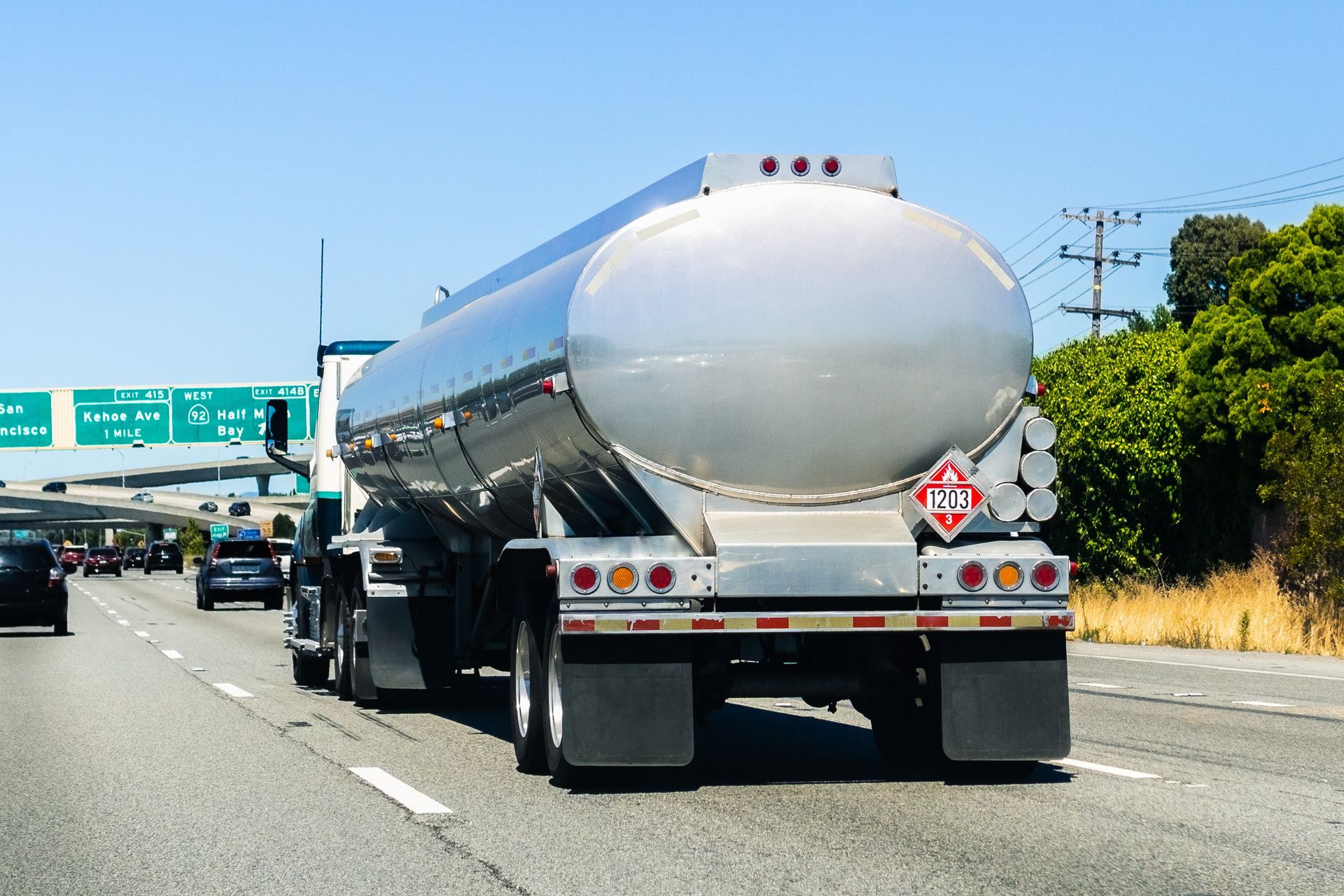 Fuel tanker truck transporting hazardous material on highway freeway with traffic, rear view driving.