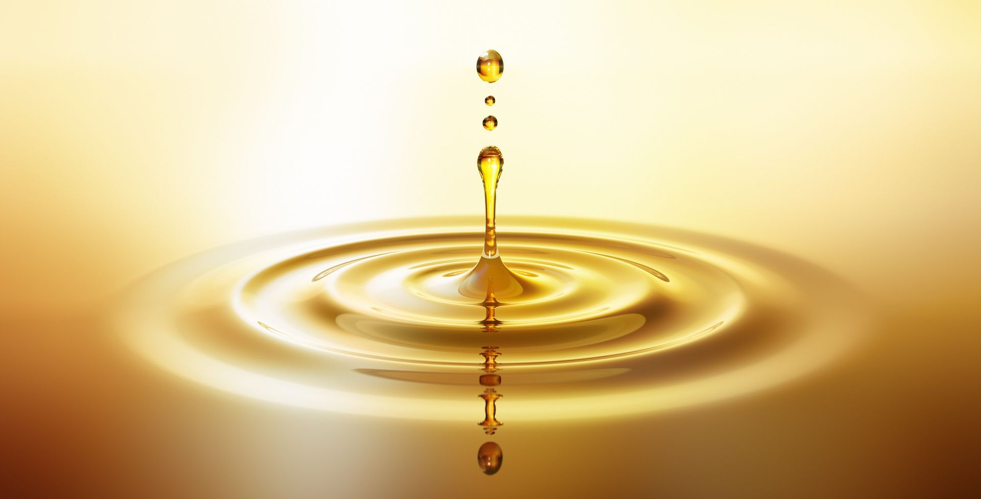 Golden water droplet splashing into calm water, creating concentric ripples on a warm yellow background
