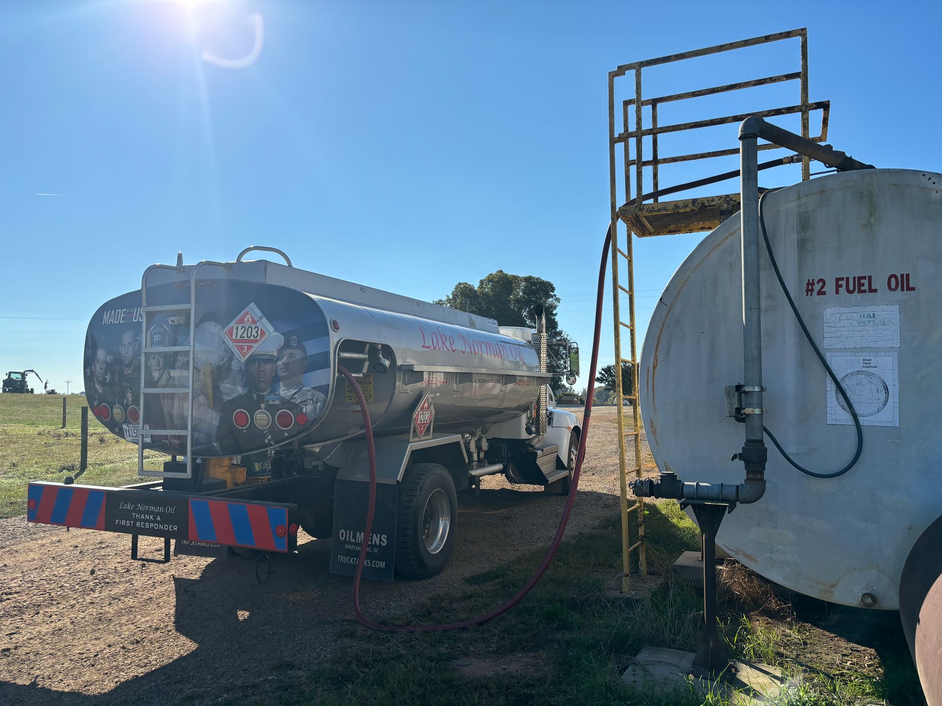 Two fuel tanker trucks parked outdoors in bright sunlight, one silver and one white.