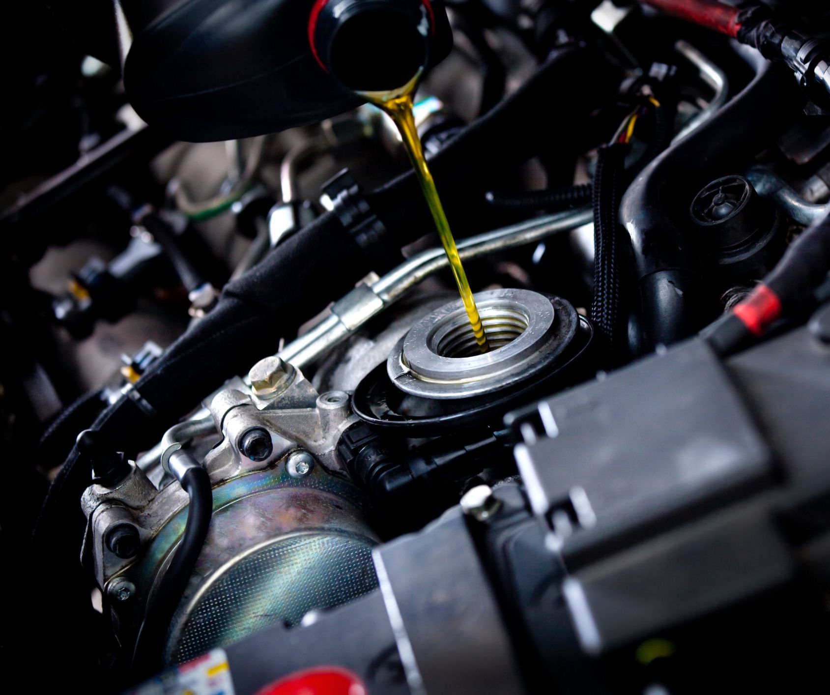 A close up of a person pouring oil into a car engine