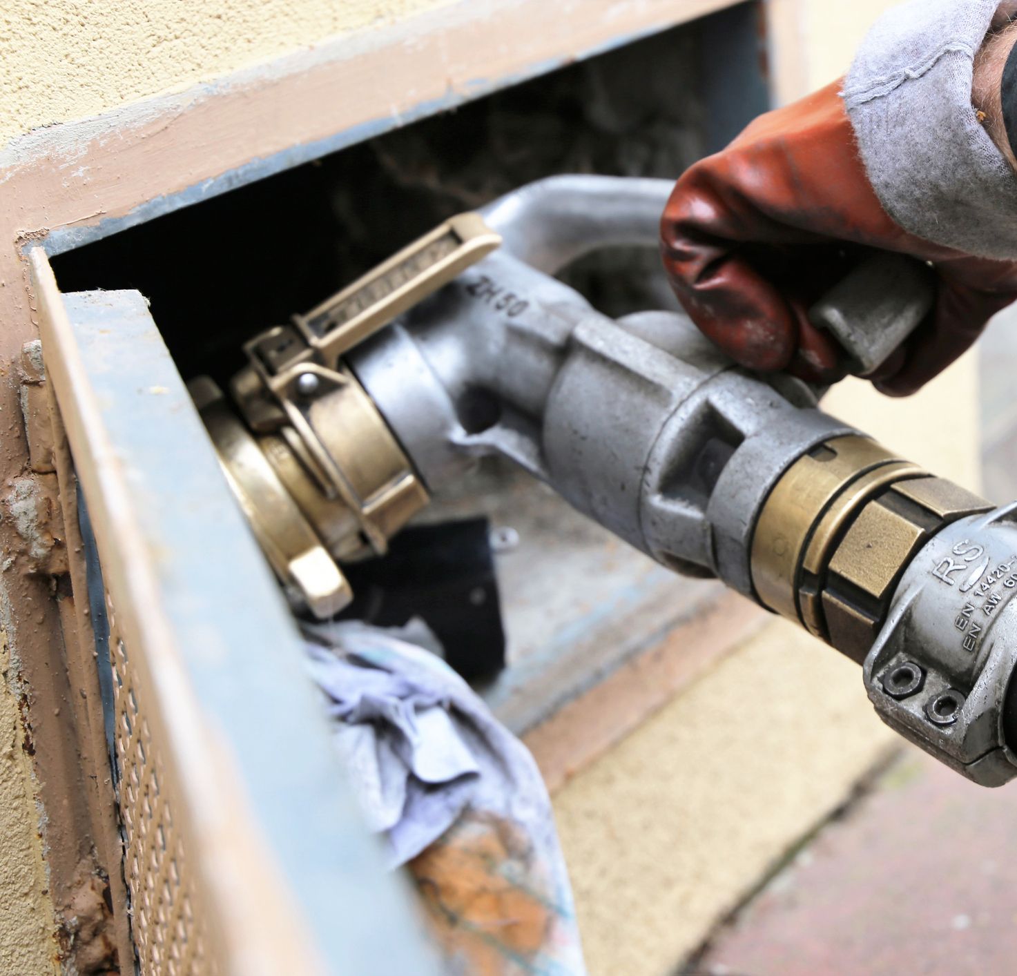 Gloved hand connecting a hose to a wall water inlet with a brass fitting
