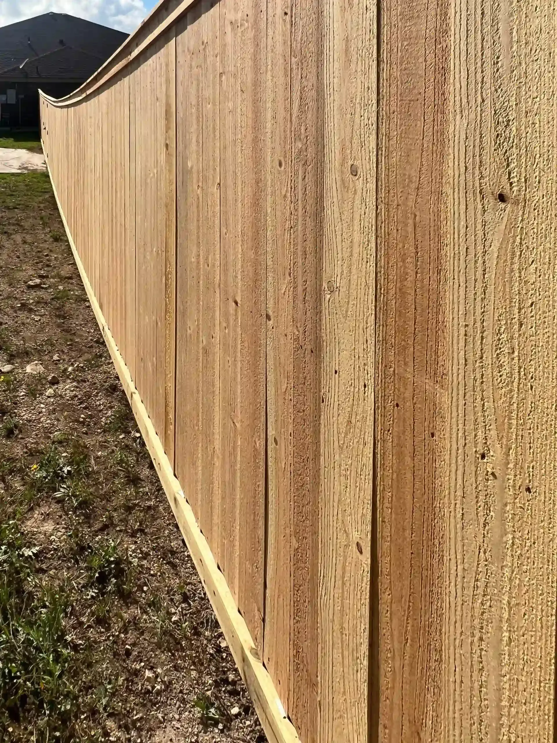 Wooden fence with a slight curve, set in a grassy yard, under a partly cloudy sky.